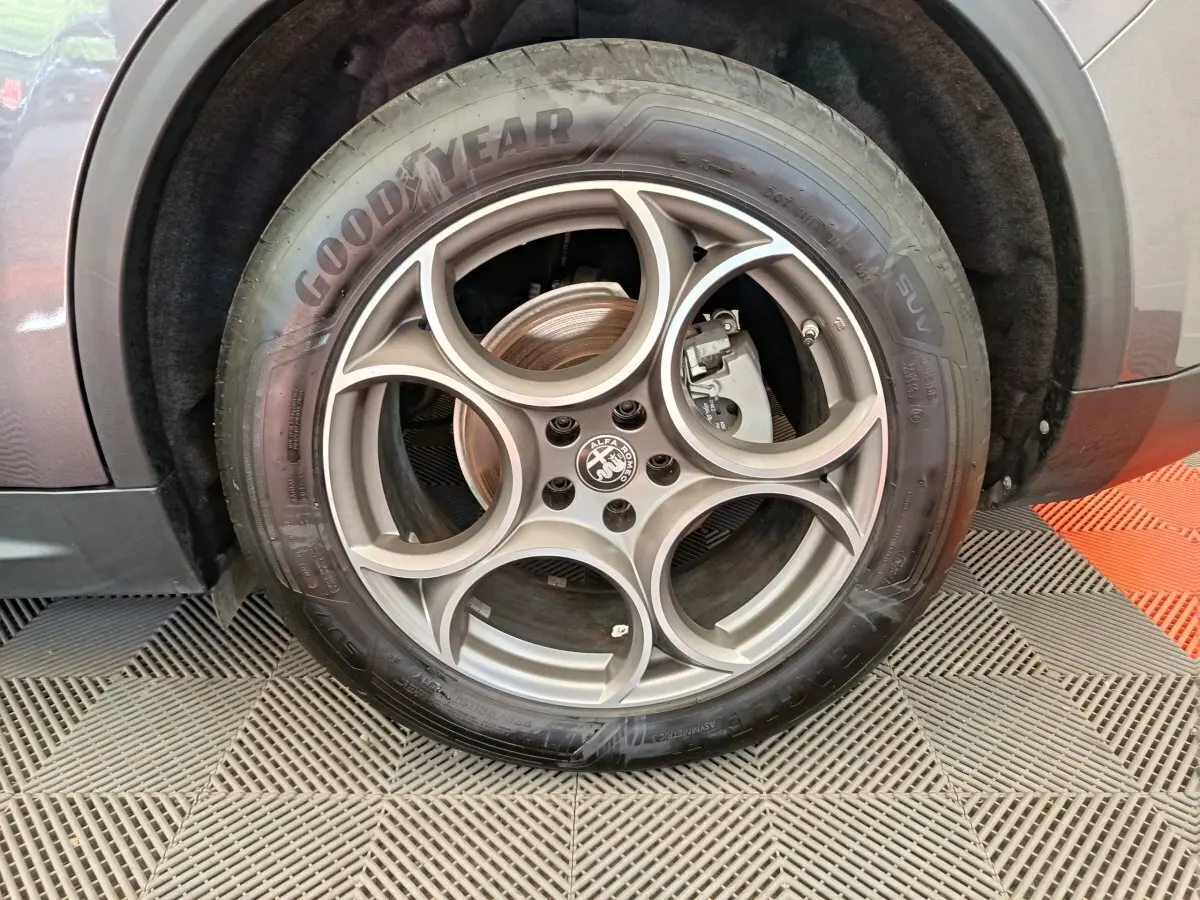 Gros plan sur la roue arrière droite d'un Alfa Romeo Stelvio gris foncé, montrant le passage de roue et le pneu.