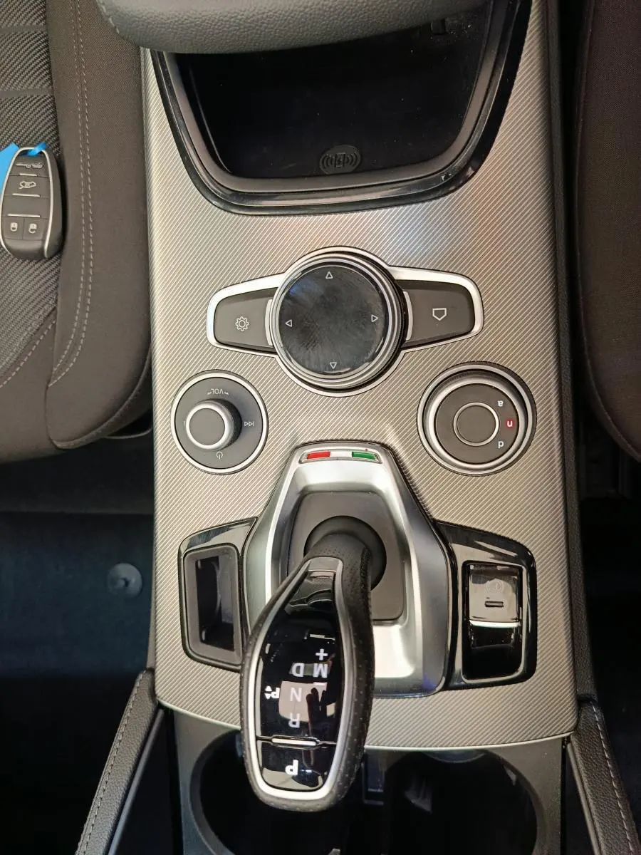 Vue plongeante sur la console centrale gris foncé de l'Alfa Romeo Stelvio avec levier de vitesses automatique et commandes rotatives.