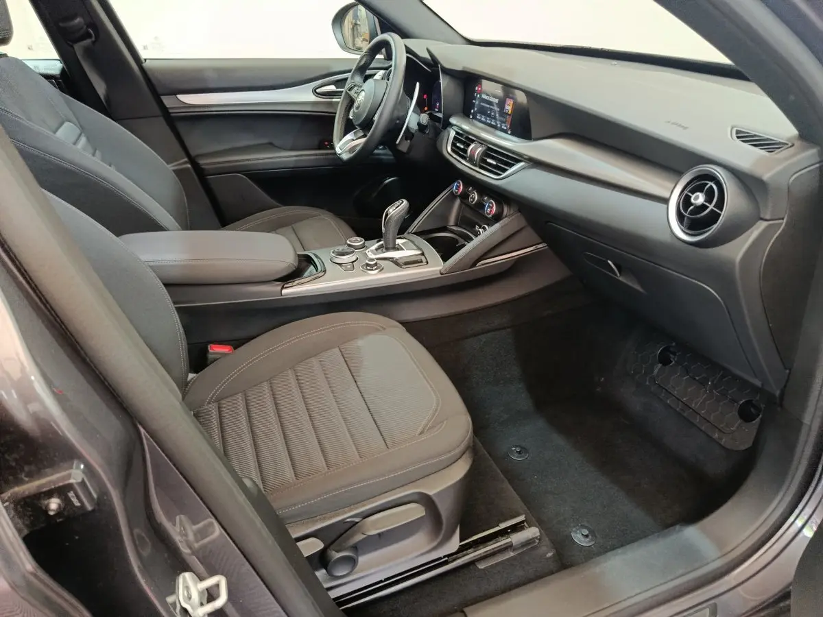 Intérieur côté passager de l'Alfa Romeo Stelvio gris foncé 2024, avec tableau de bord moderne et sièges tissu noirs.