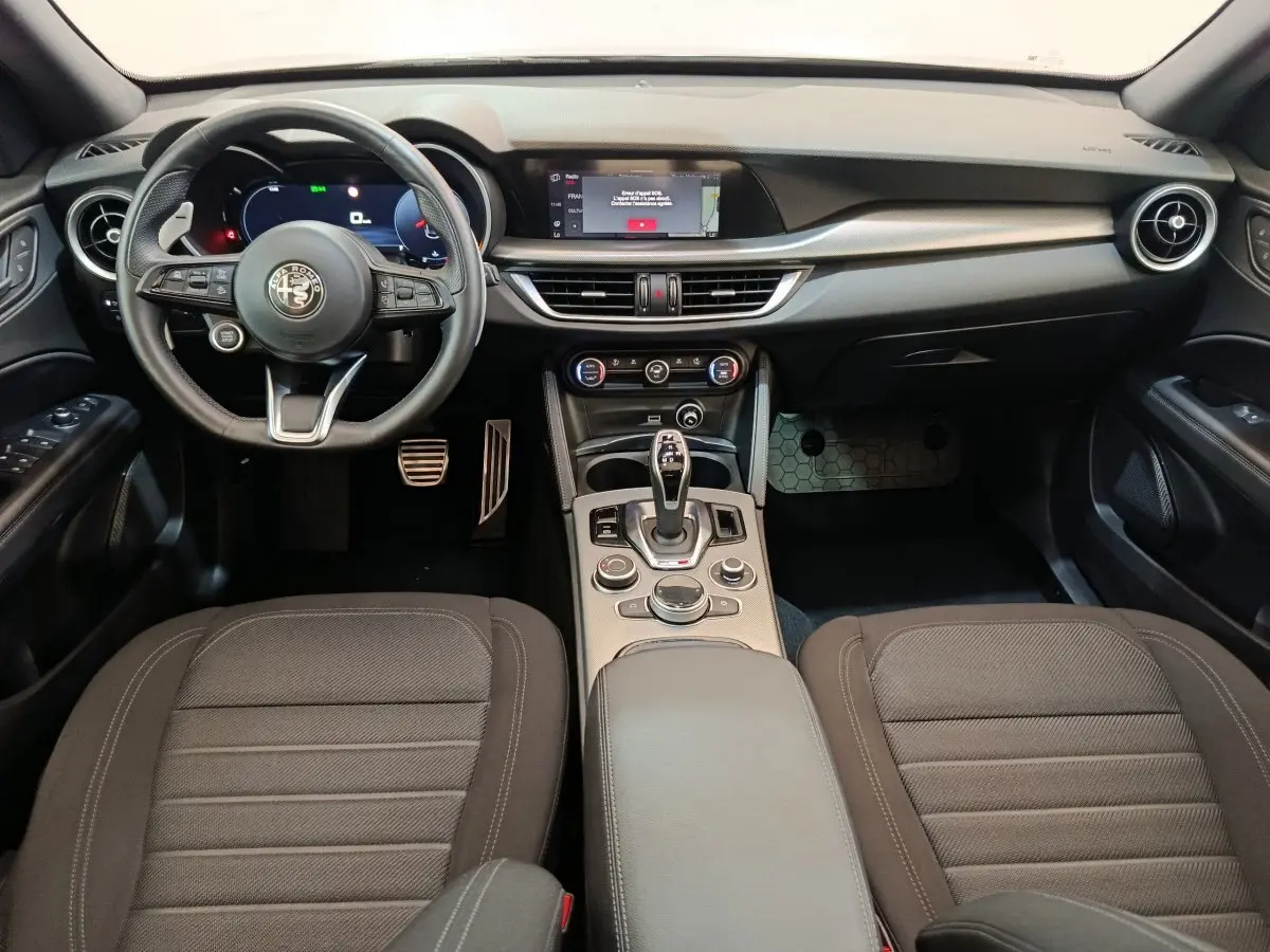Vue intérieure avant de l'Alfa Romeo Stelvio Sprint 2024, tableau de bord noir avec écran tactile et volant cuir multifonctions.