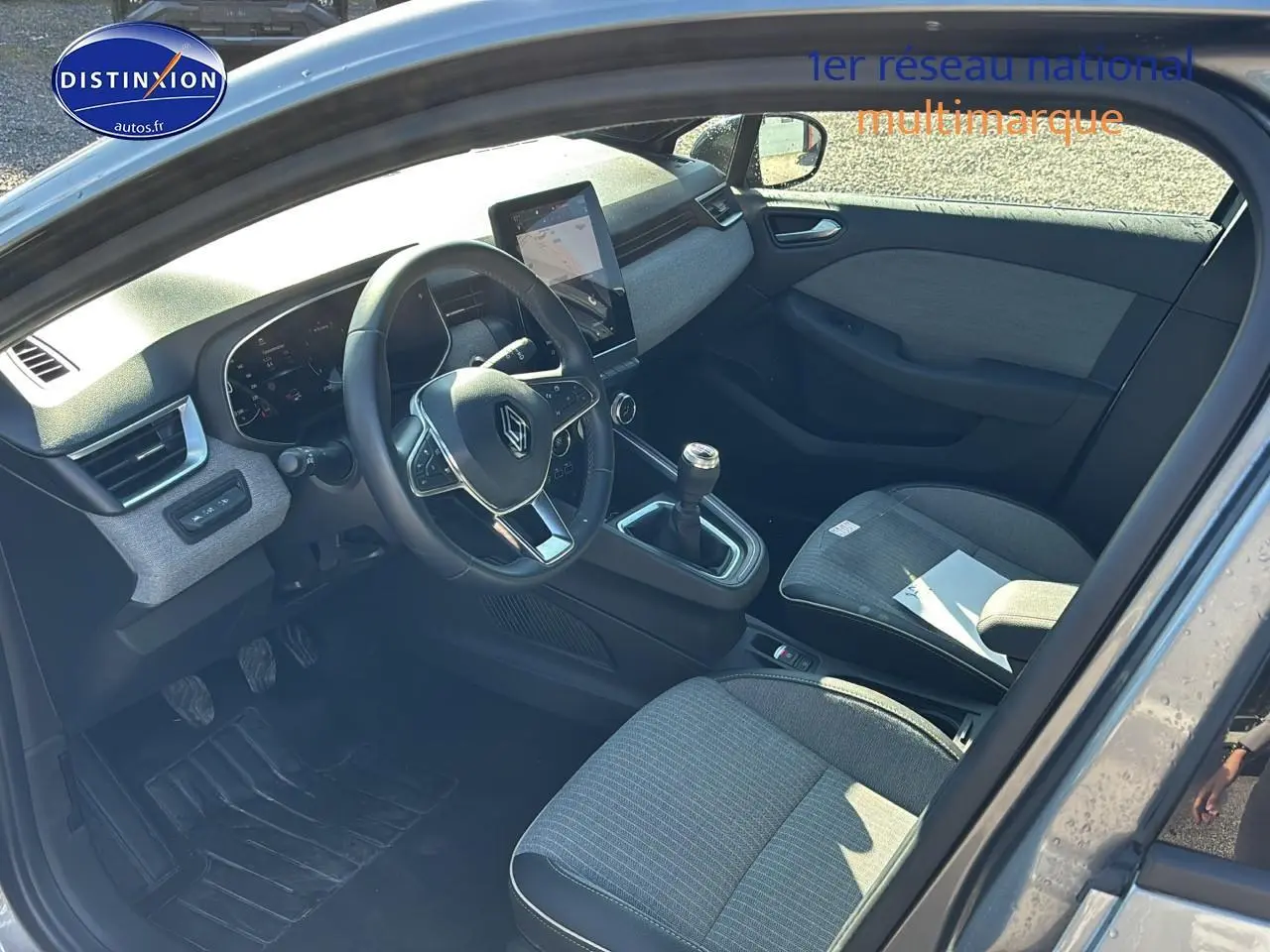 Intérieur avant droit d'une Renault Clio V gris pizzara, volant textile, boîte manuelle et écran tactile central visible.