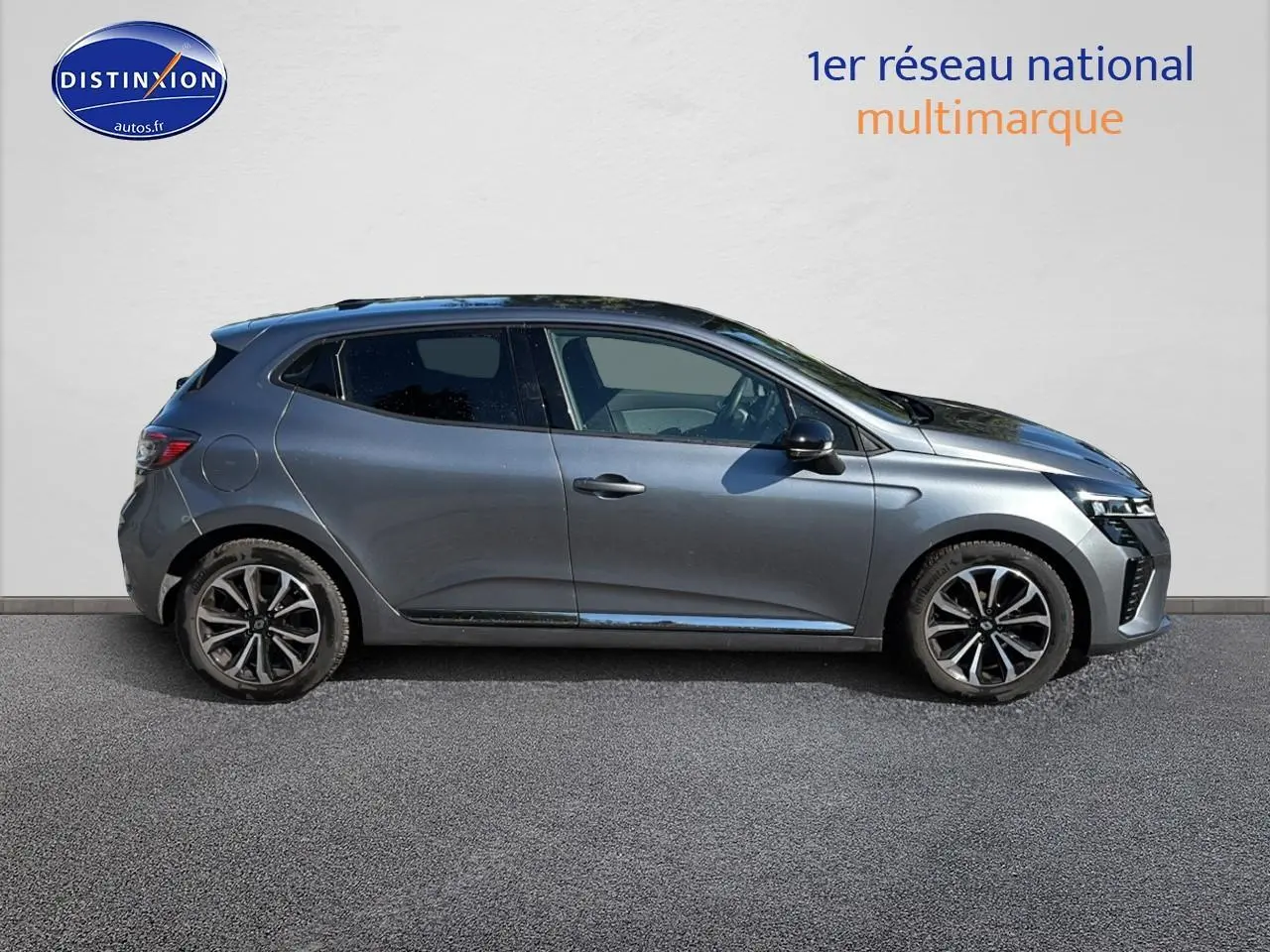 Profil droit d'une Renault Clio V gris pizzara avec jantes alliage noires et calandre chromée visible sur fond clair.