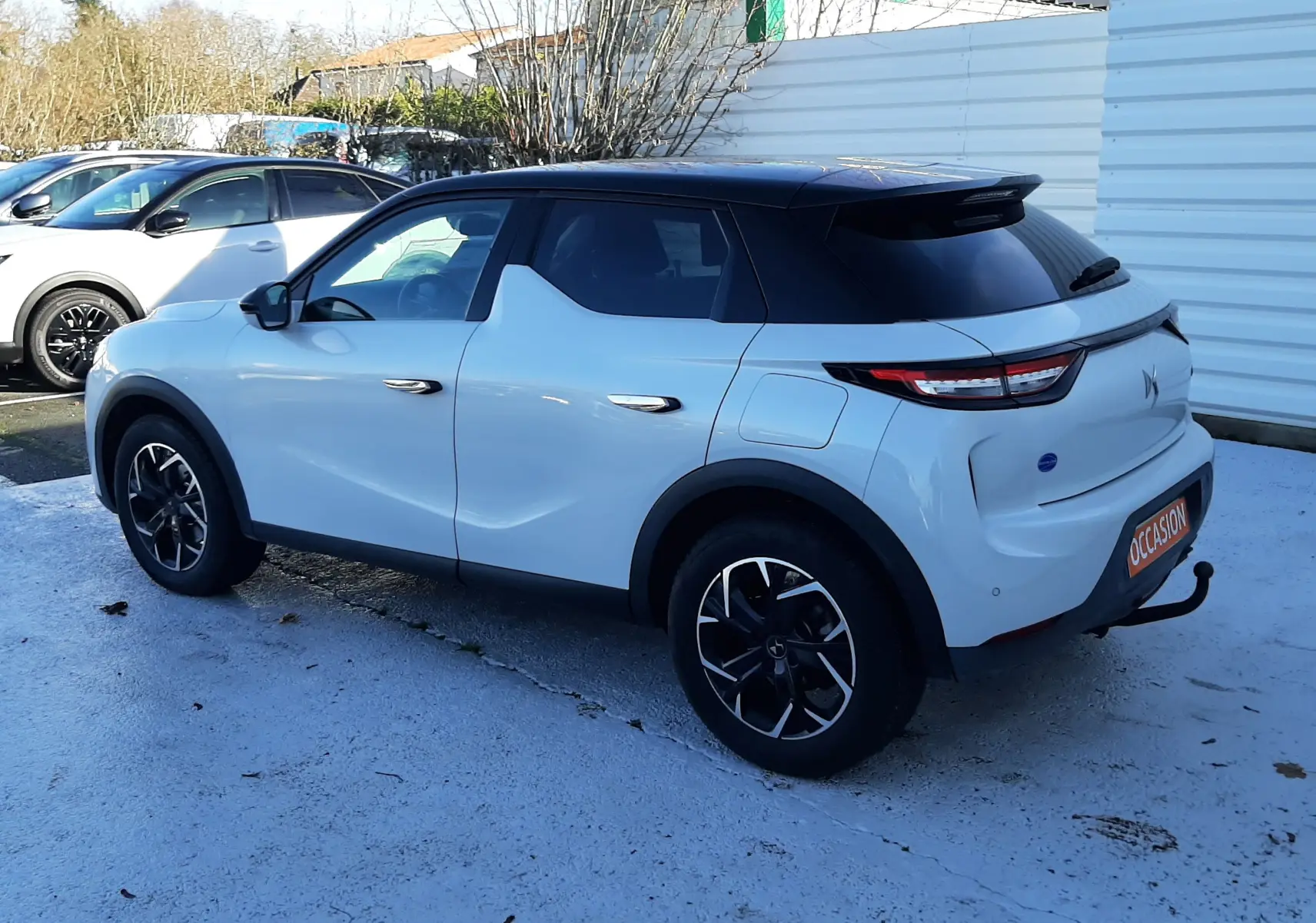 Vue 3/4 arrière droite d'un DS3 Crossback blanc perle avec toit noir, jantes noires et feux arrière LED distinctifs.