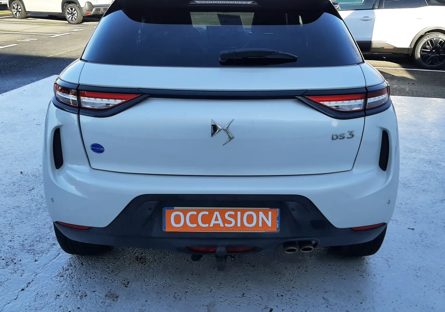 Vue arrière d'une DS3 Crossback blanc perle avec toit noir, plaque orange "OCCASION" visible sur un parking.