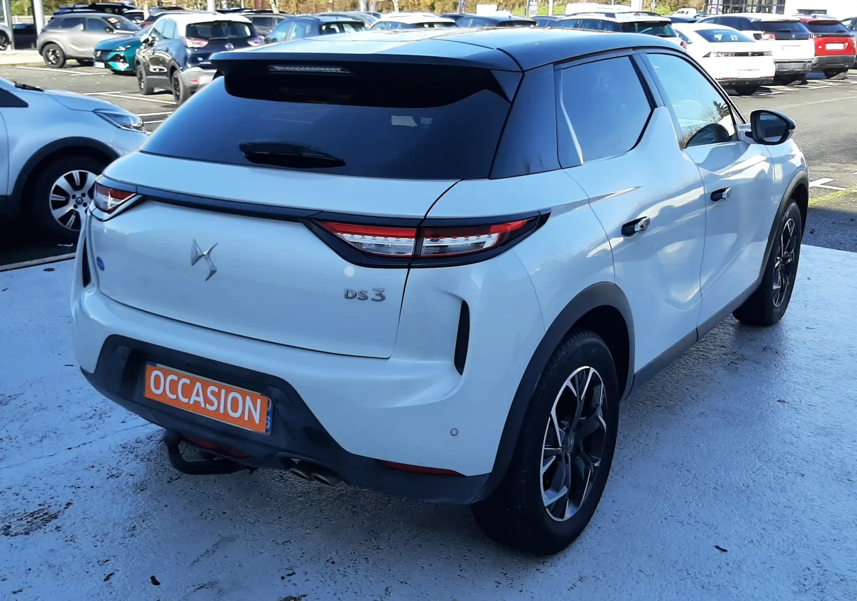 Vue 3/4 arrière droite d'un DS3 Crossback blanc perle avec toit noir et jantes noires en stationnement.