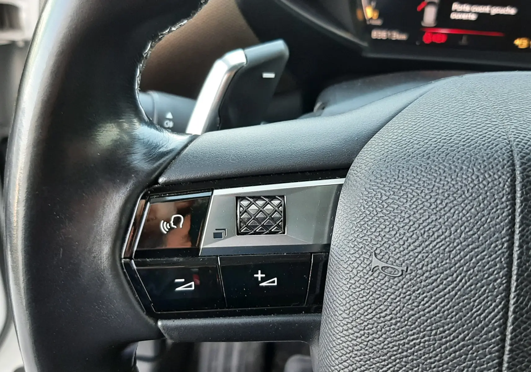 Gros plan sur les commandes du volant en cuir noir du DS3 Crossback 2019, avec affichage numérique en arrière-plan.