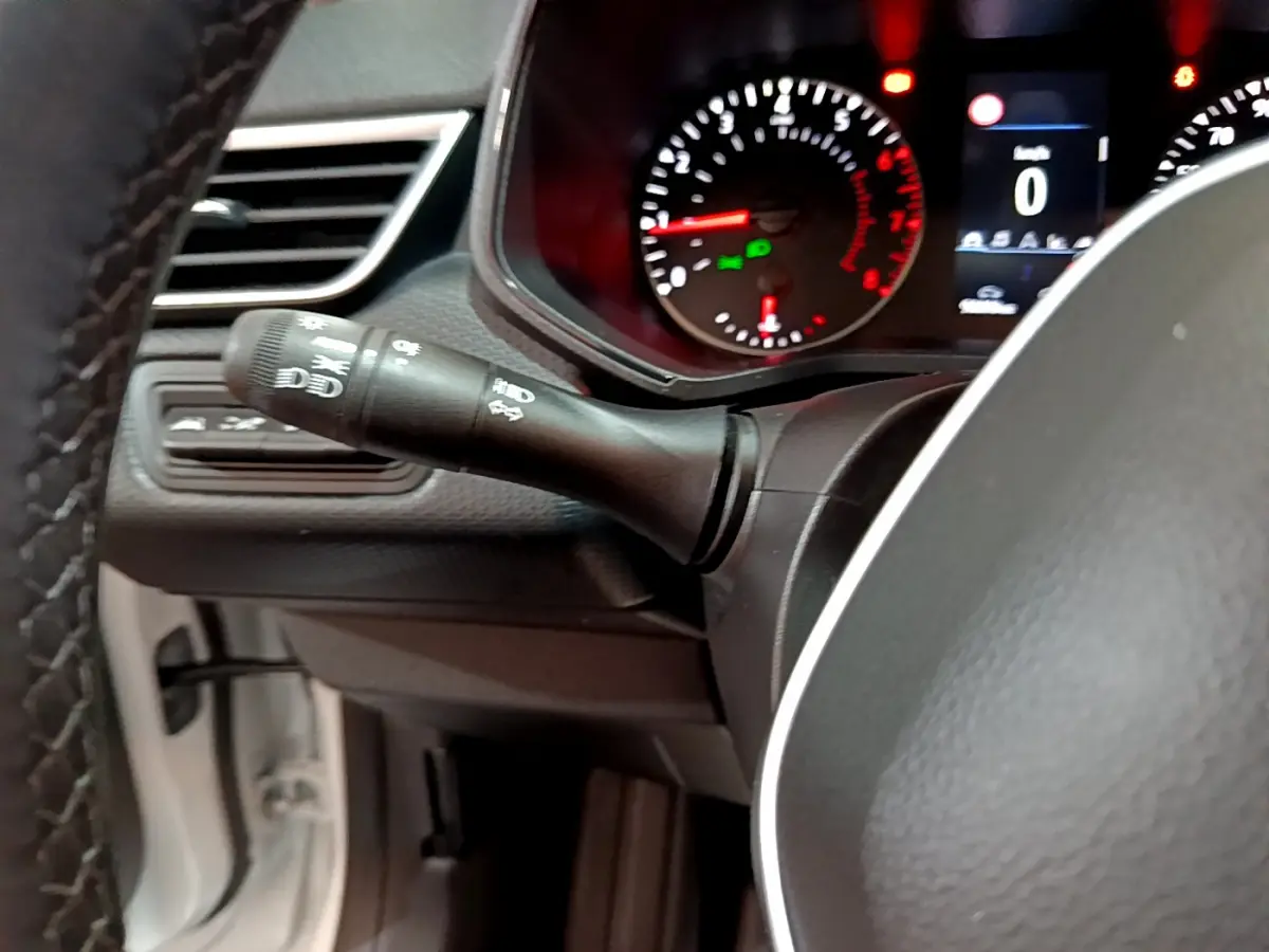 Gros plan sur le commodo gauche et le tableau de bord éclairé de la Renault Clio Business blanche, affichant le compteur à zéro.