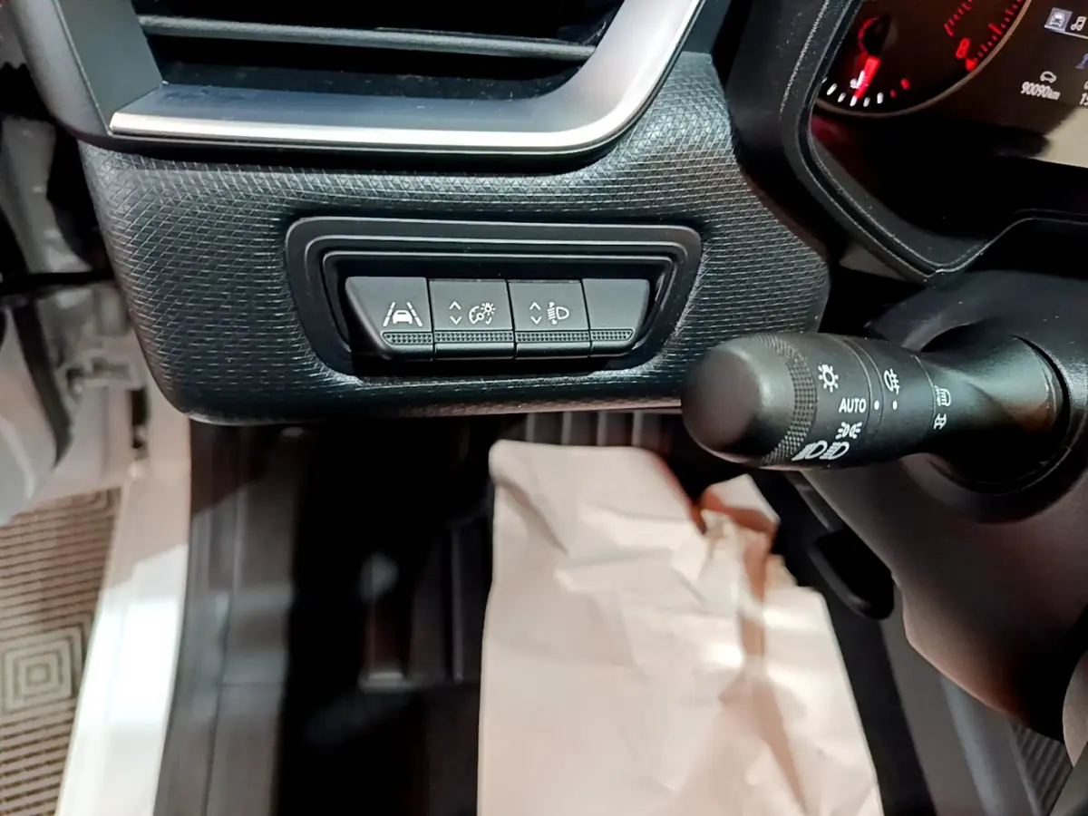 Gros plan sur les commandes d'assistance et éclairage côté gauche du tableau de bord d'une Renault Clio blanche 2021.