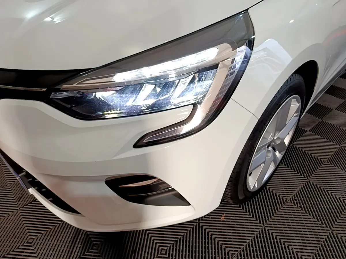 Gros plan sur le phare avant droit allumé d'une Renault Clio Business TCe 90 blanche, avec jante alu visible.
