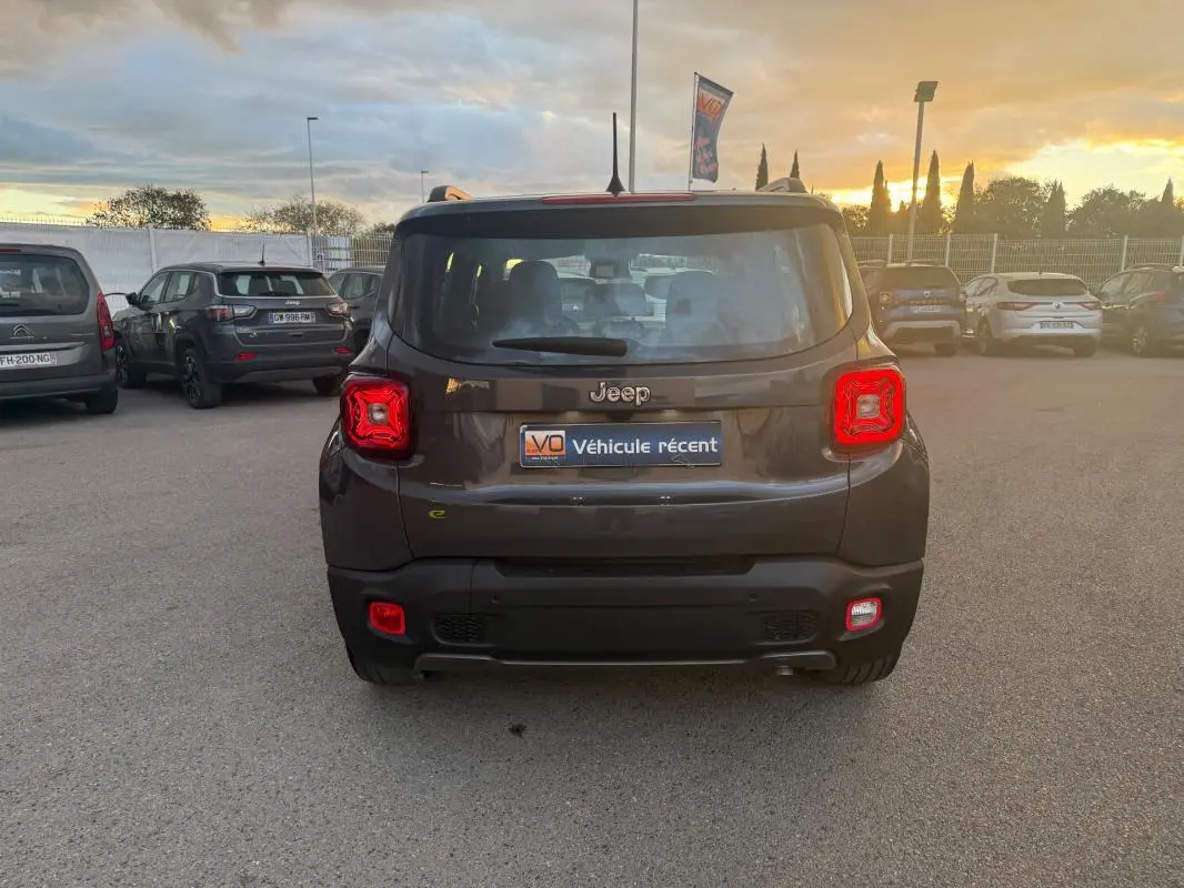 Vue arrière d'un Jeep Renegade gris anthracite 2024 avec feux arrière allumés sur un parking au coucher du soleil.