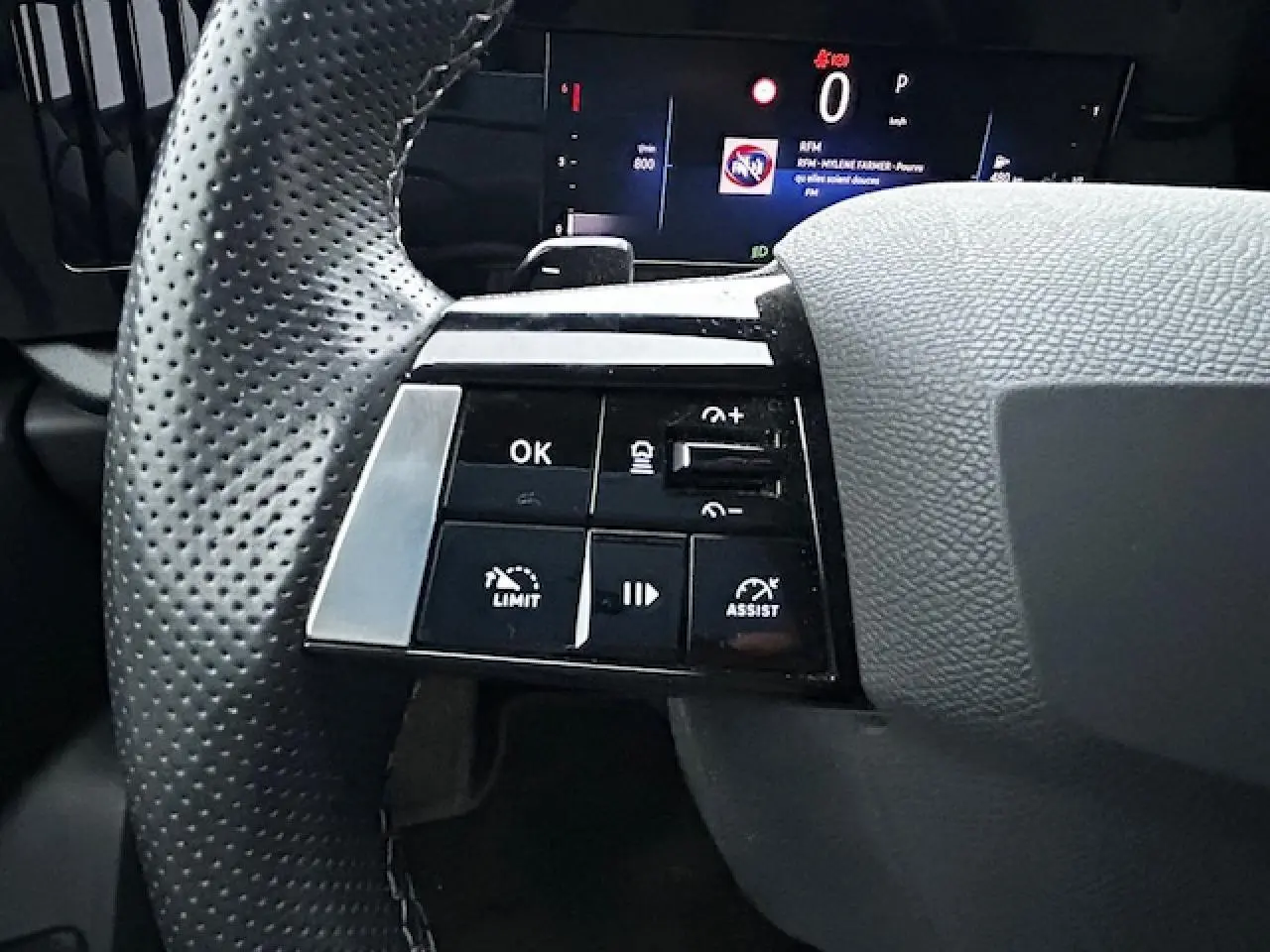 Gros plan sur les commandes gauche du volant cuir perforé de l'Opel Astra VI Diesel 2022 avec affichage numérique.