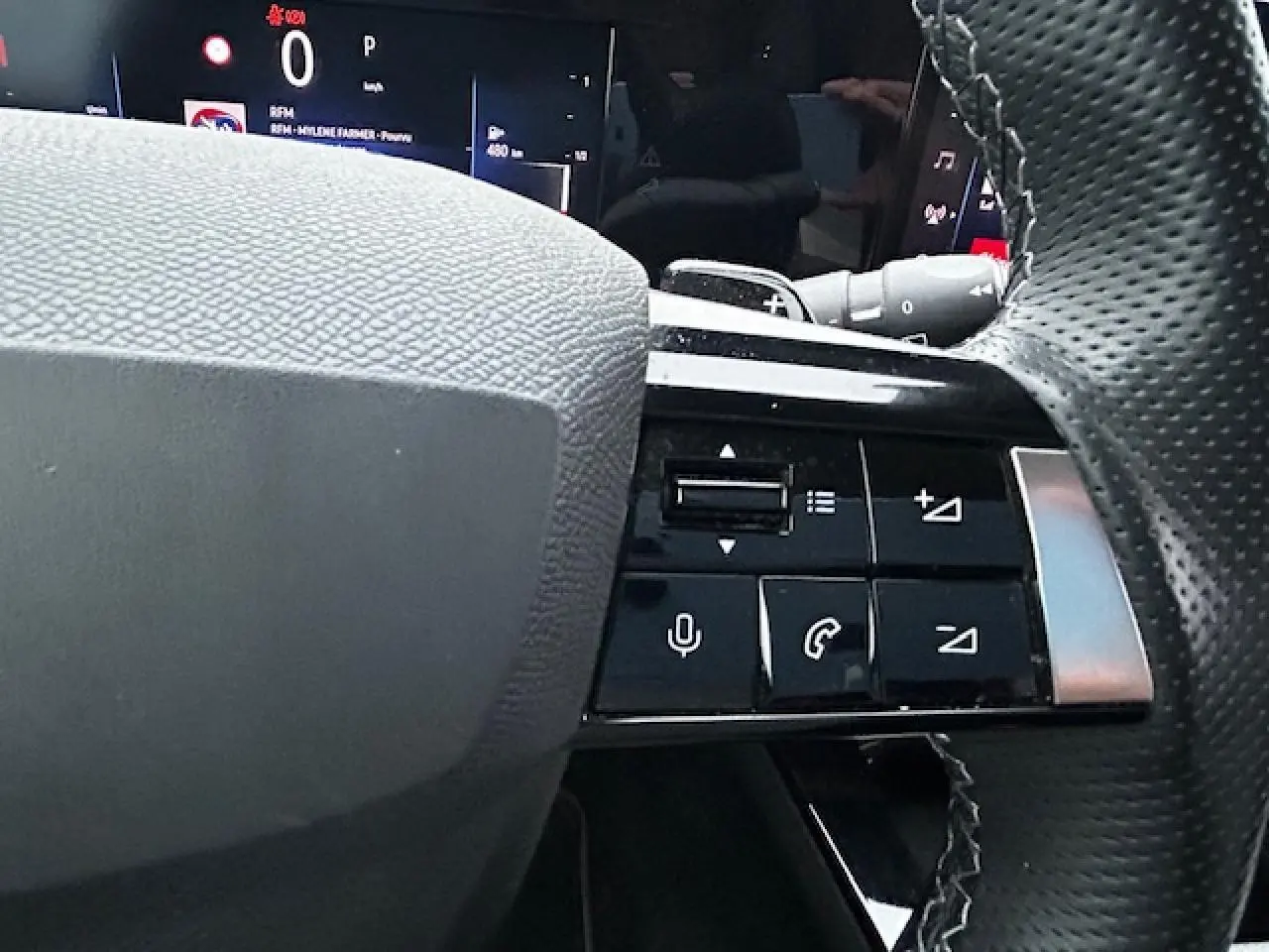 Gros plan sur les commandes au volant cuir premium de l'Opel Astra VI diesel 2022, avec affichage numérique en arrière-plan.