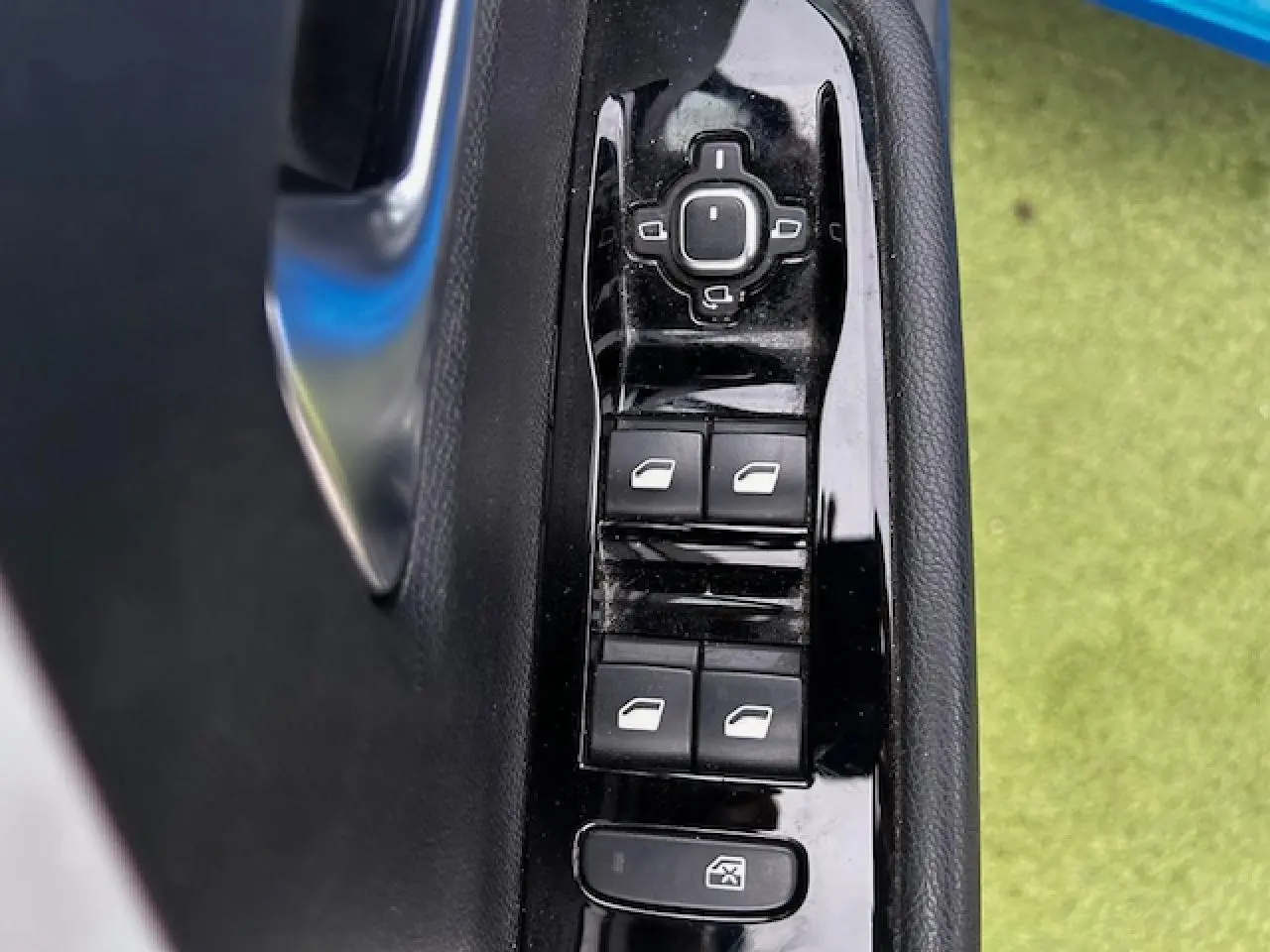 Gros plan sur les commandes de lève-vitres et rétroviseurs sur la porte côté gauche d'une Opel Astra bleu clair.