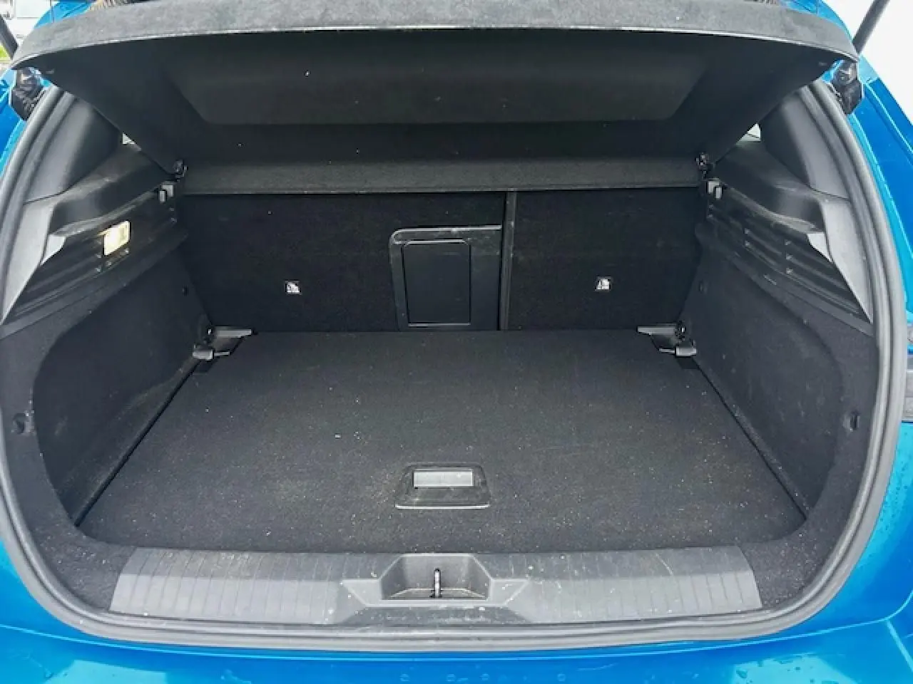 Coffre ouvert de l'Opel Astra bleu clair, vue arrière montrant l'espace de chargement et la trappe à skis intégrée.