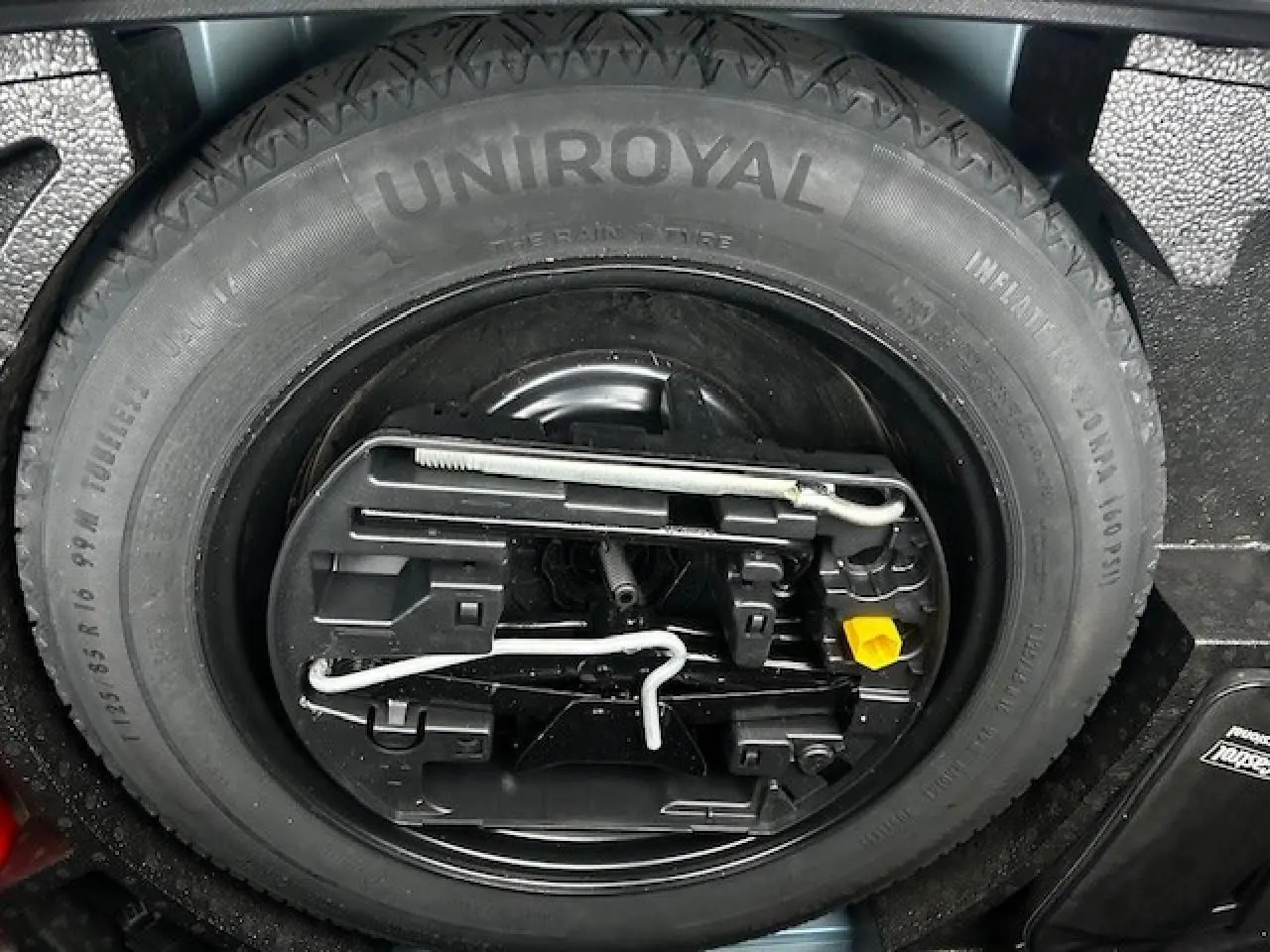 Gros plan sur la roue de secours Uniroyal et son kit d'outils dans le coffre d'une Opel Astra bleu clair 2022.