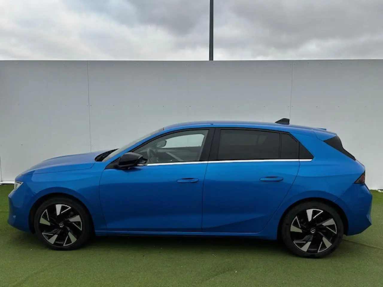 Profil latéral droit d'une Opel Astra VI bleu clair avec jantes alliage noires et vitres surteintées.
