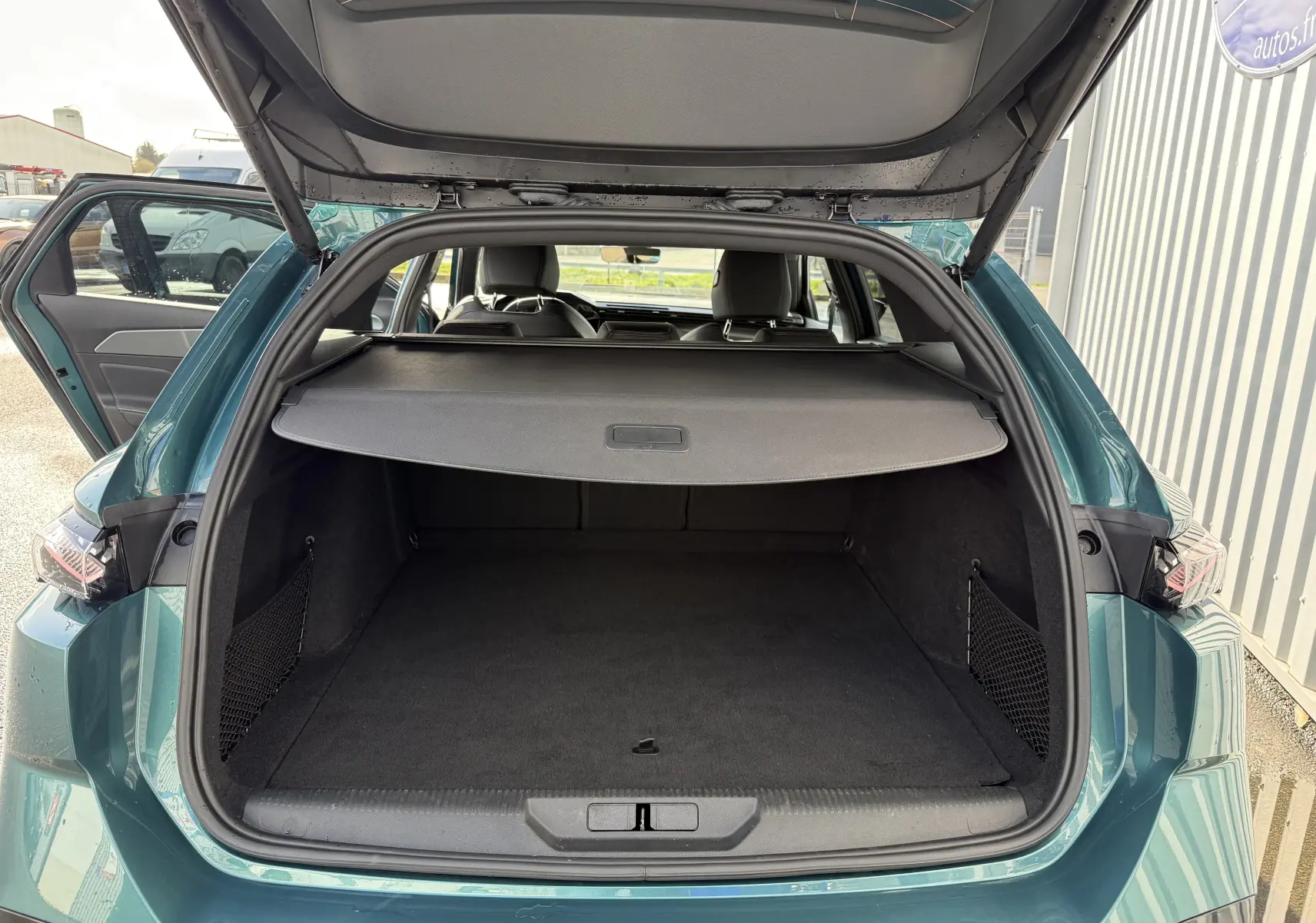 Coffre ouvert vu de l'arrière d'une Peugeot 308 SW Bleu Avartar, montrant l'espace de chargement avec cache-bagages déployé.