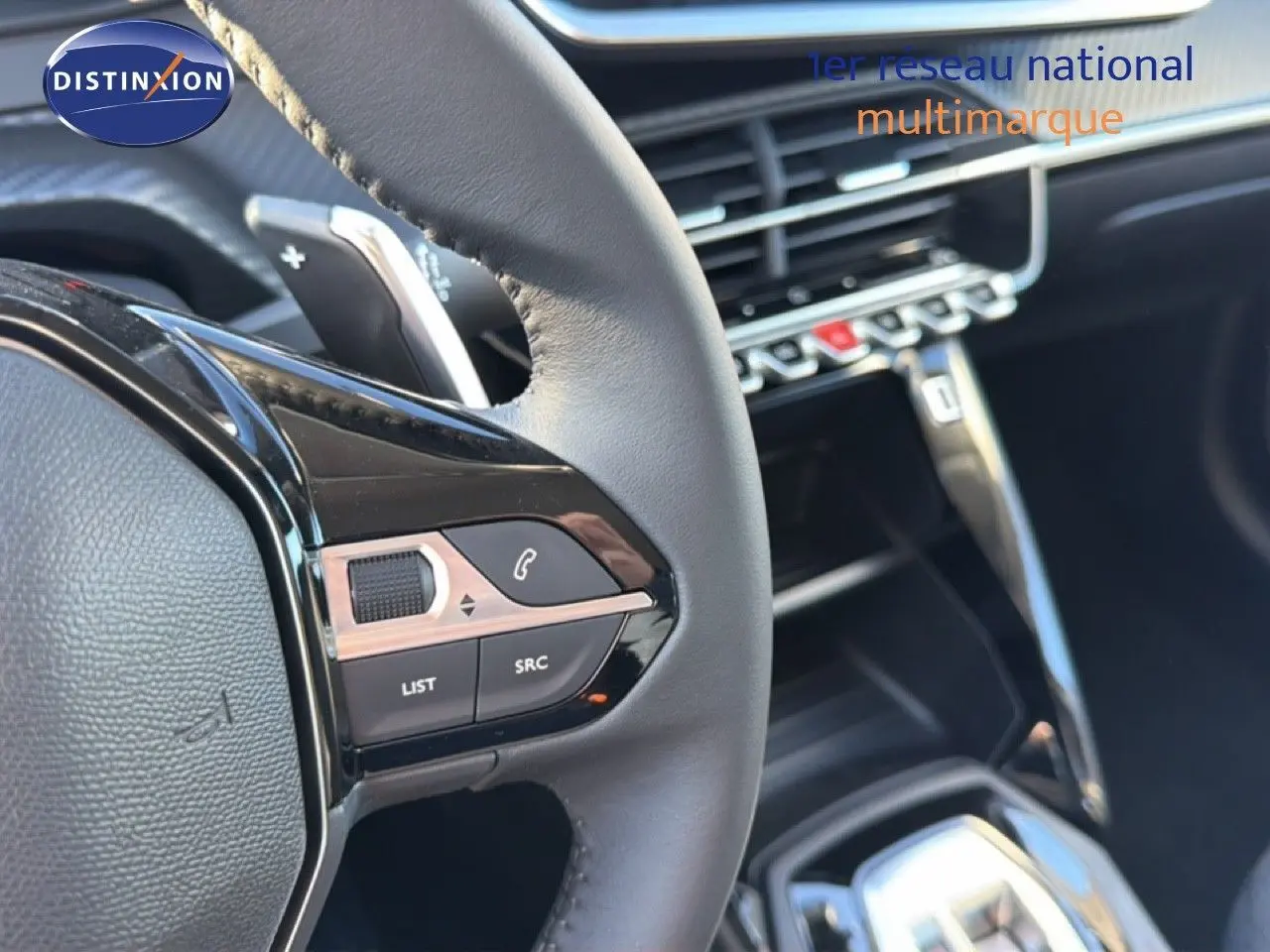 Gros plan sur le volant cuir noir et les commandes multimédia de la Peugeot 208 hybride 2025, intérieur moderne