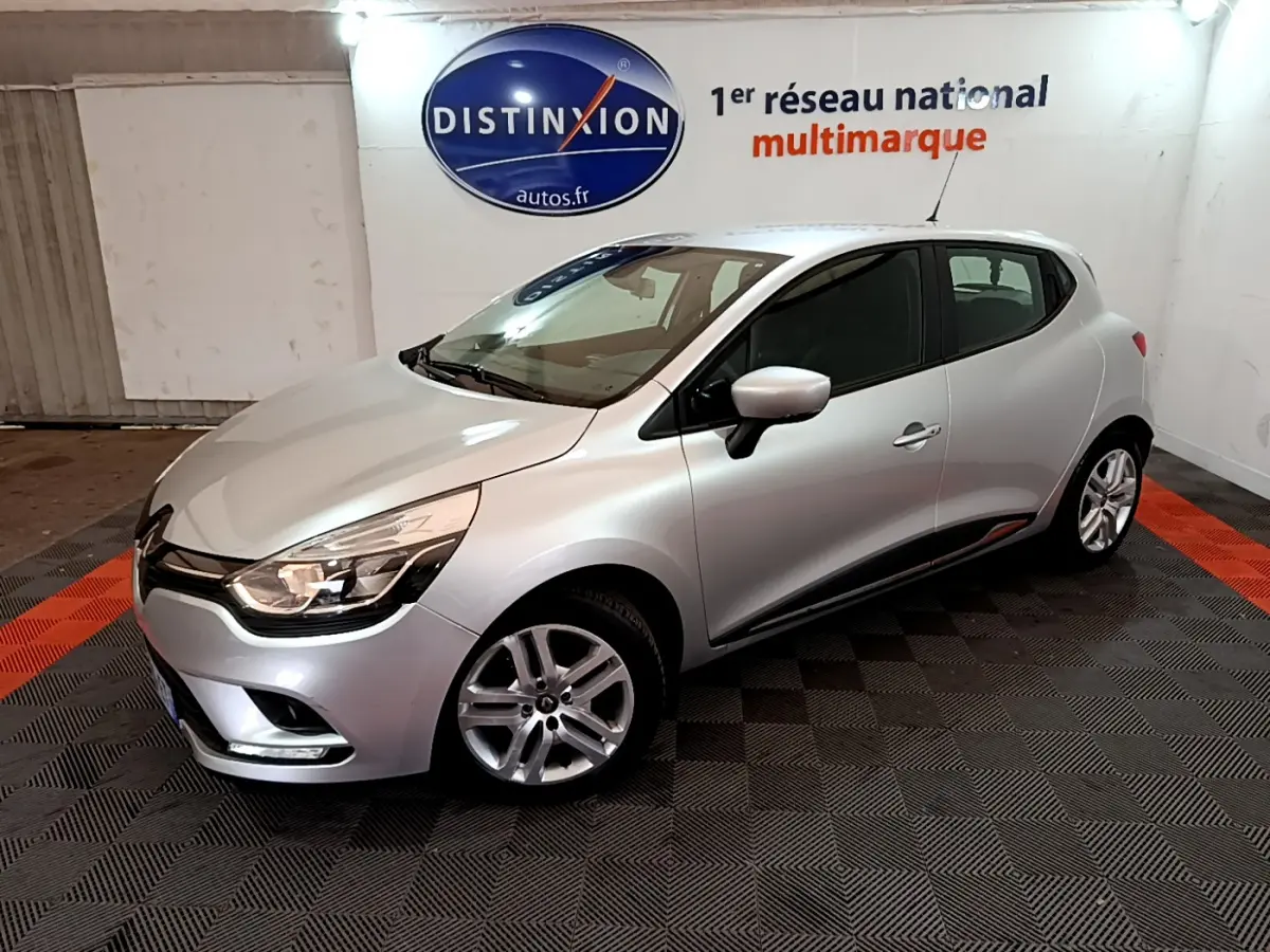 Renault Clio Business TCe 90 gris clair vue 3/4 avant droit dans un showroom avec logo Distinxion en arrière-plan