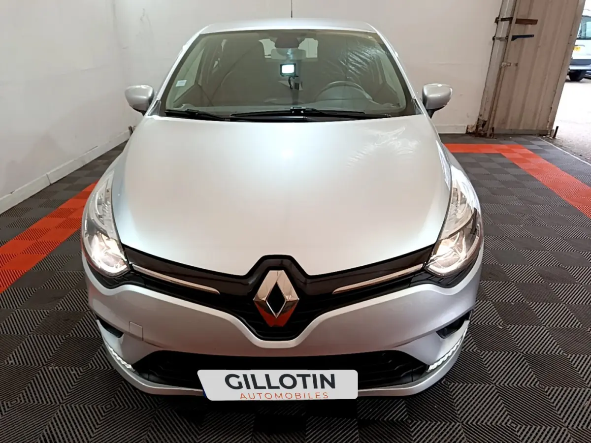 Vue avant d'une Renault Clio Business TCe 90 gris clair avec phares allumés dans un garage.