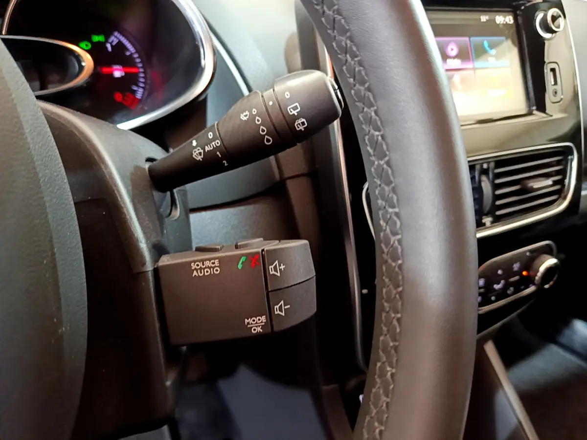 Vue rapprochée côté gauche du volant cuir de la Renault Clio Business gris clair, avec commandes audio et écran tactile visible.