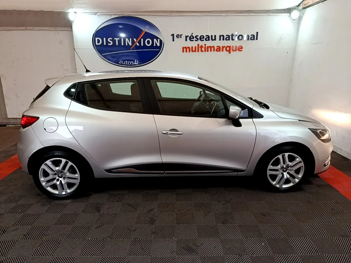 Renault Clio Business TCe 90 gris clair vue de profil côté droit en intérieur avec jantes alliage et feux allumés.