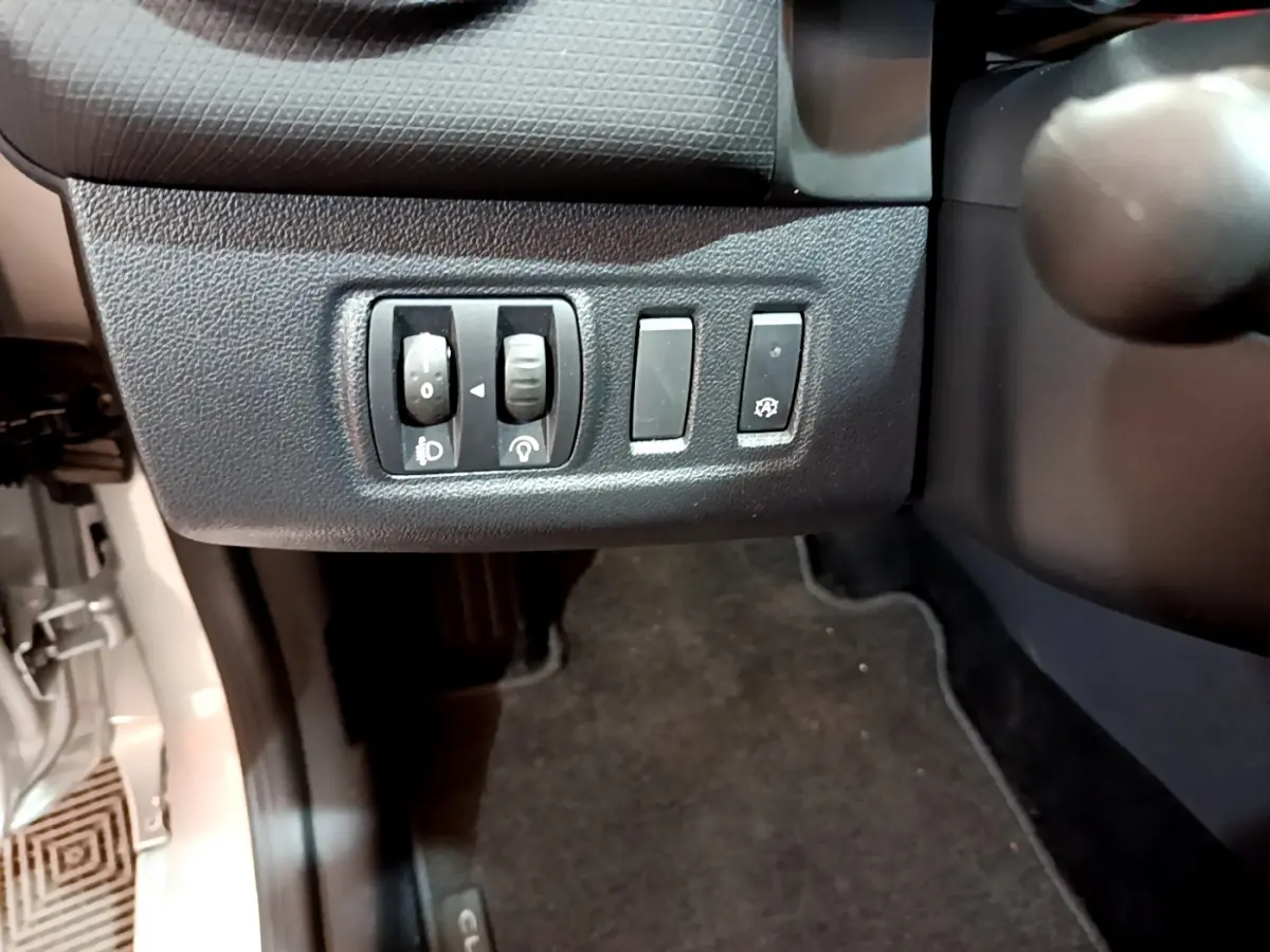 Gros plan sur les commandes de réglage des phares et autres boutons à gauche du volant dans une Renault Clio Business gris clair 2019.