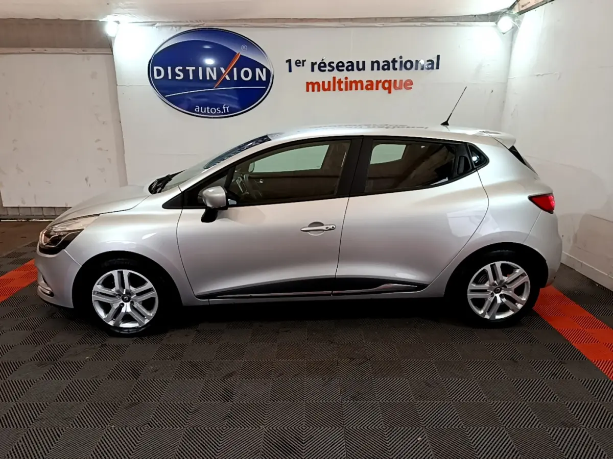 Profil côté gauche d'une Renault Clio Business TCe 90 gris clair, stationnée en intérieur sur sol à damier noir et rouge.