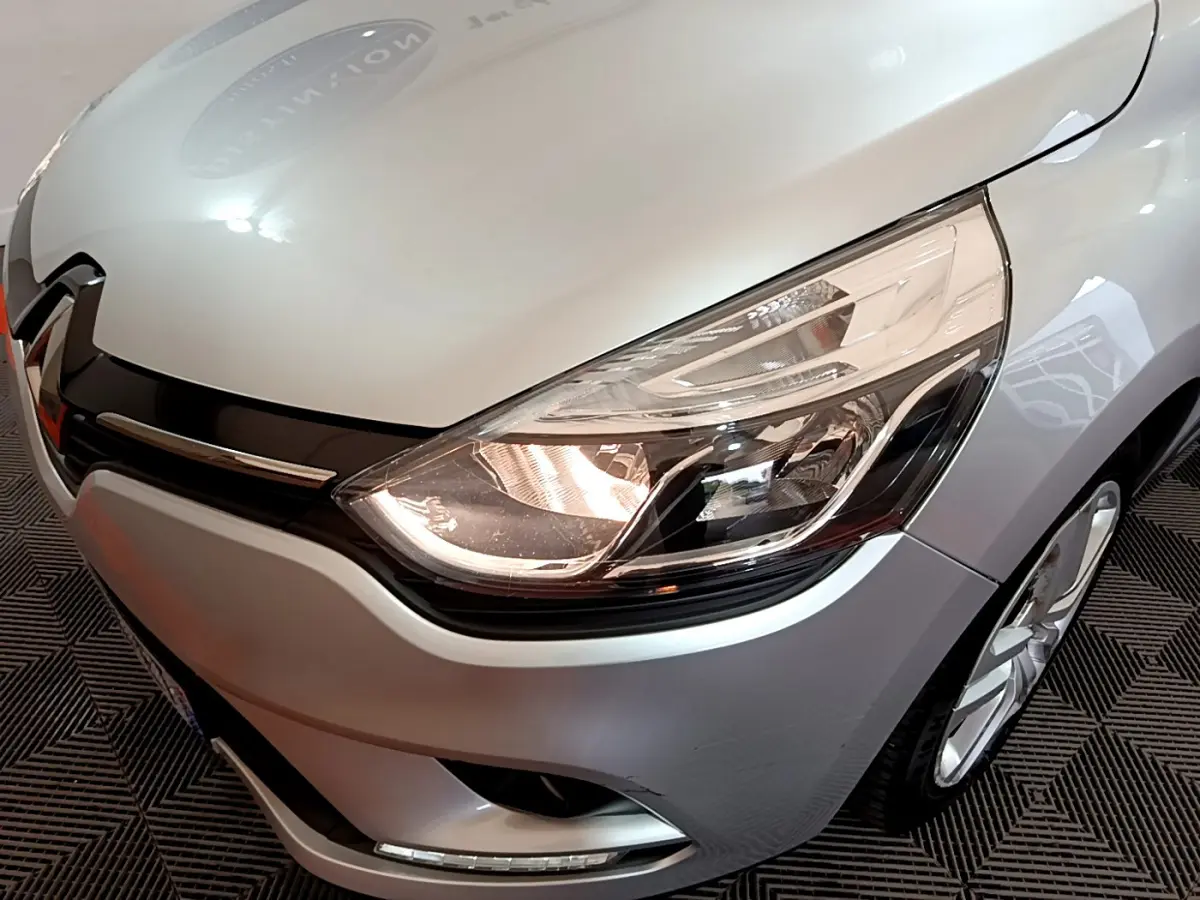 Gros plan sur l'avant droit gris clair de la Renault Clio 2019, mettant en valeur le phare et la calandre noire brillante.