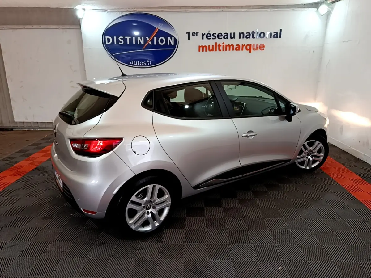 Renault Clio Business TCe 90 gris clair vue 3/4 arrière droit dans un showroom avec logo Distinxion en arrière-plan.