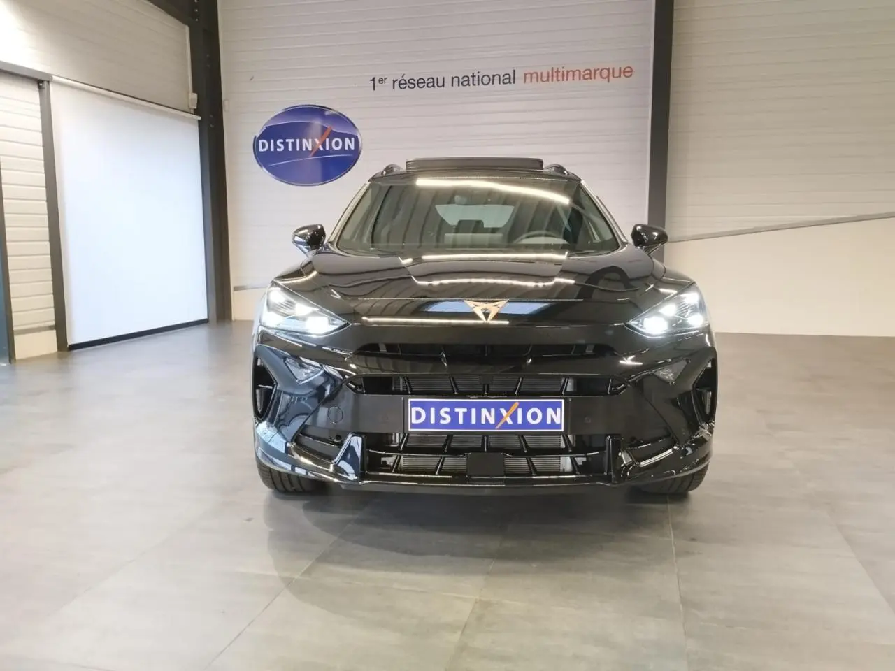 Vue frontale d'un CUPRA Formentor noir métal 2026 avec logo cuivré et phares LED allumés en intérieur showroom.