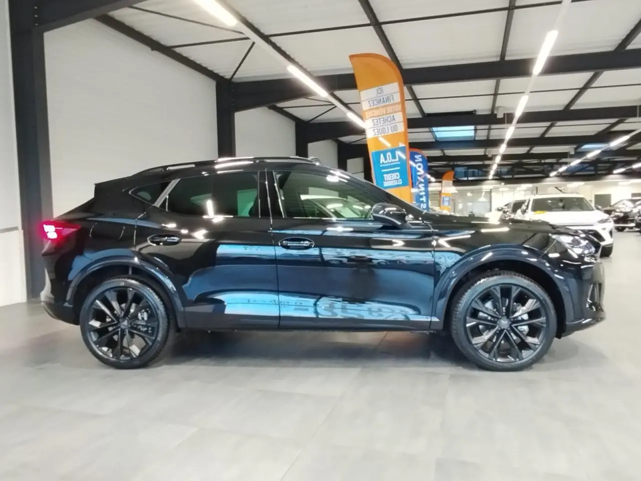 Vue latérale gauche d'un CUPRA Formentor noir métal avec jantes alliage noires et toit ouvrant panoramique en intérieur showroom.