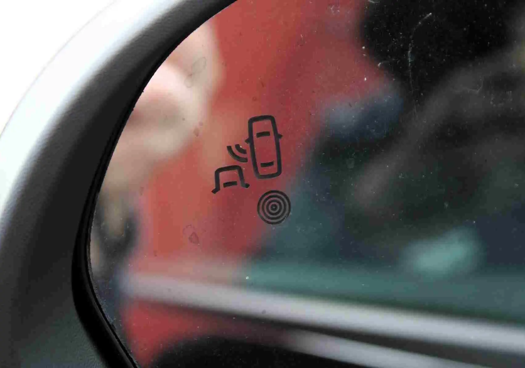 Gros plan sur le rétroviseur gauche du Dacia Duster noir avec icône d'alerte d'angle mort visible.