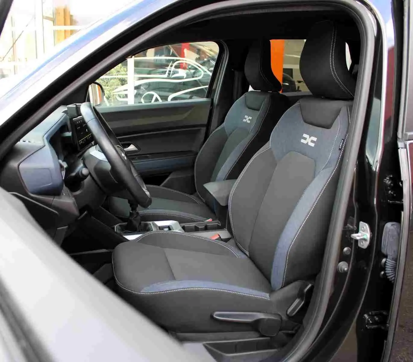 Vue intérieure côté conducteur du Dacia Duster noir 2025, mettant en valeur les sièges avant Denim avec logo Dacia.