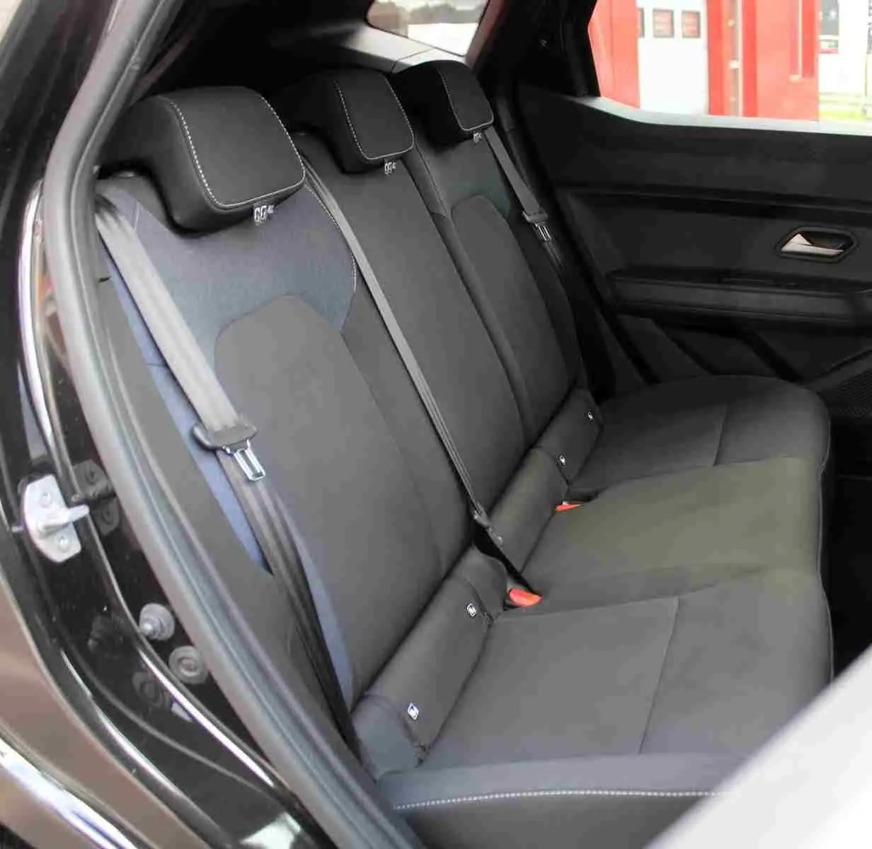 Vue latérale intérieure montrant la banquette arrière noire avec appuie-têtes et ceintures dans un Dacia Duster 2025.