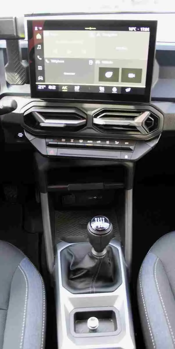 Vue intérieure centrée sur la console centrale et levier de vitesses manuelle du Dacia Duster 2025, sellerie Denim Bleu.
