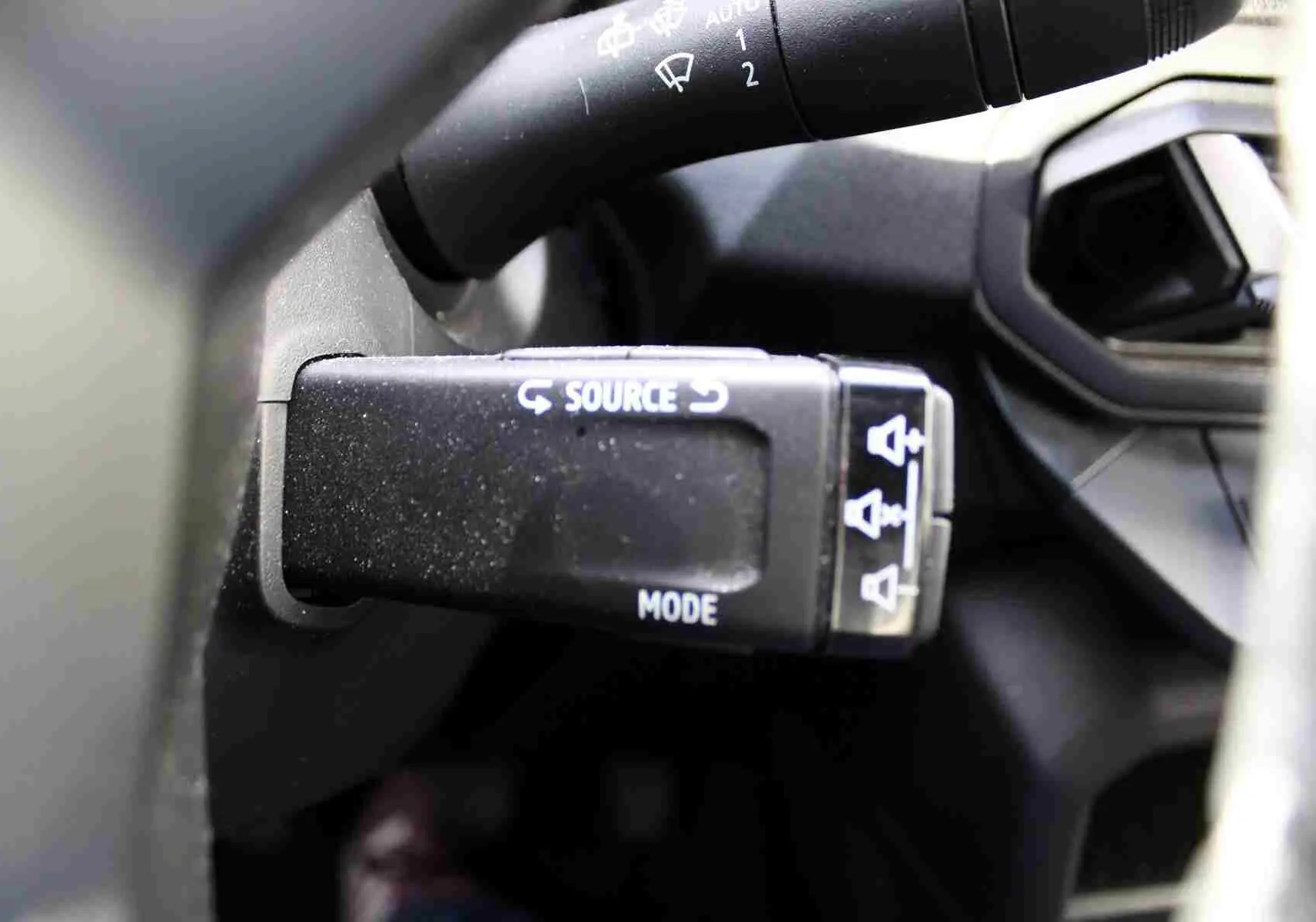 Gros plan sur la commande au volant noire du Dacia Duster 2025, avec inscriptions blanches "SOURCE" et "MODE".