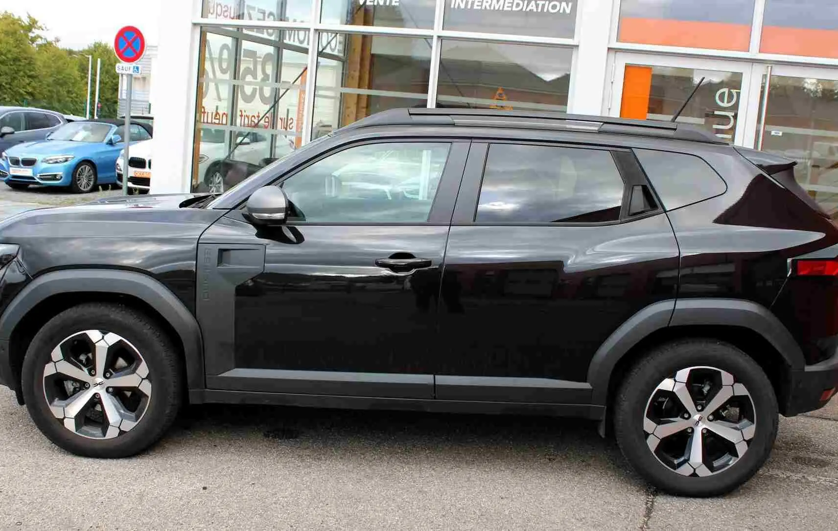 Vue de profil côté gauche d'un Dacia Duster noir nacré 2025 avec jantes alliage 18 pouces et barres de toit noires.