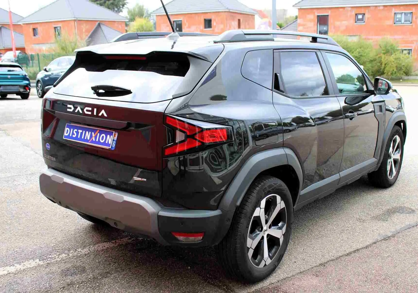 Vue 3/4 arrière droite du Dacia Duster 2025 noir nacré avec jantes alliage 18 pouces et barres de toit noires.