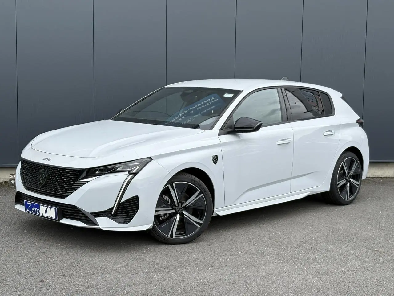 Peugeot 308 blanc Okenite vue 3/4 avant droit avec jantes alliage 18'' diamantées et calandre noire distinctive.