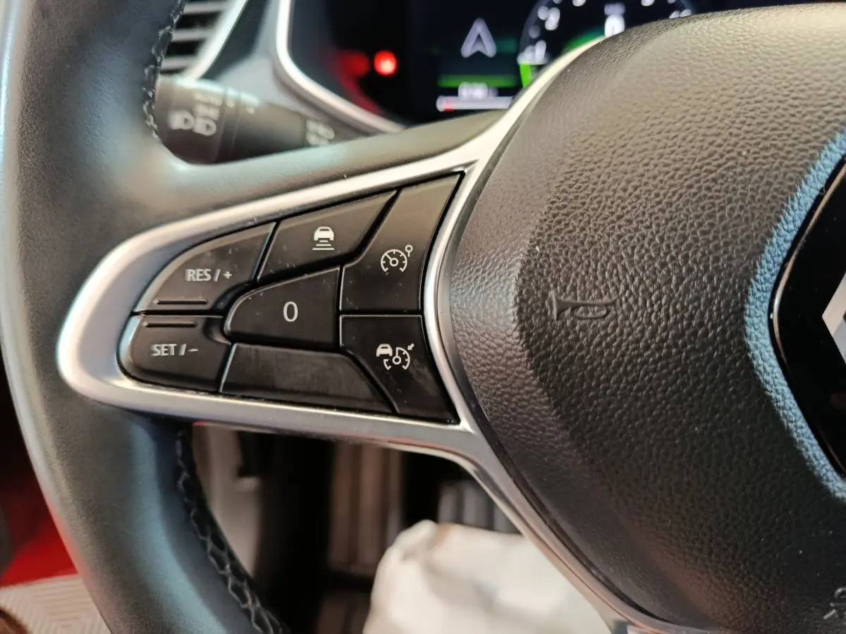 Gros plan sur les commandes à gauche du volant cuir noir de la Renault Clio Techno TCe 90 rouge 2024.