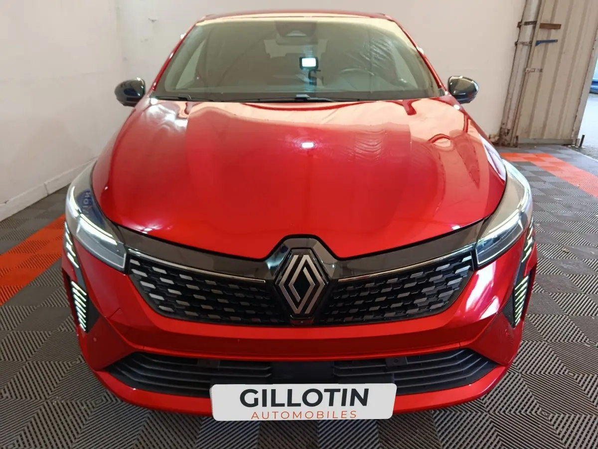 Vue frontale d'une Renault Clio Techno TCe 90 rouge avec calandre noire et feux LED allumés en intérieur.