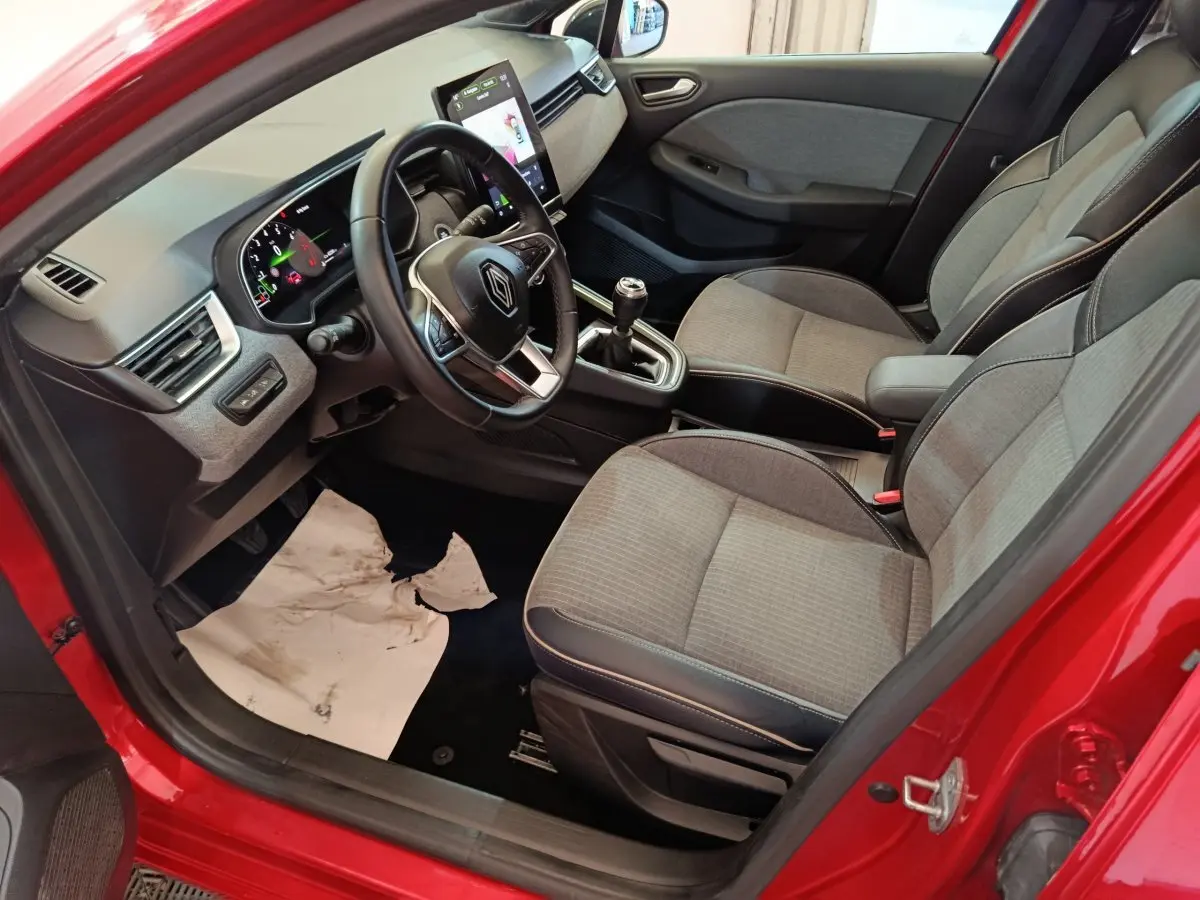 Vue intérieure côté conducteur de la Renault Clio Techno TCe 90 rouge 2024, avec tableau de bord numérique et sièges tissu gris.