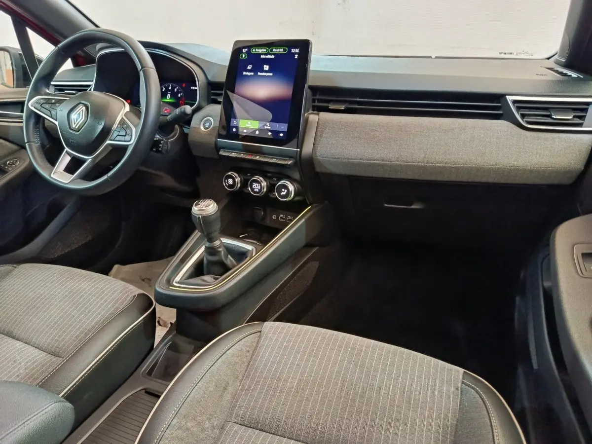 Intérieur Renault Clio Techno 2024 vu de face, volant cuir, écran tactile vertical et sellerie grise à rayures fines.