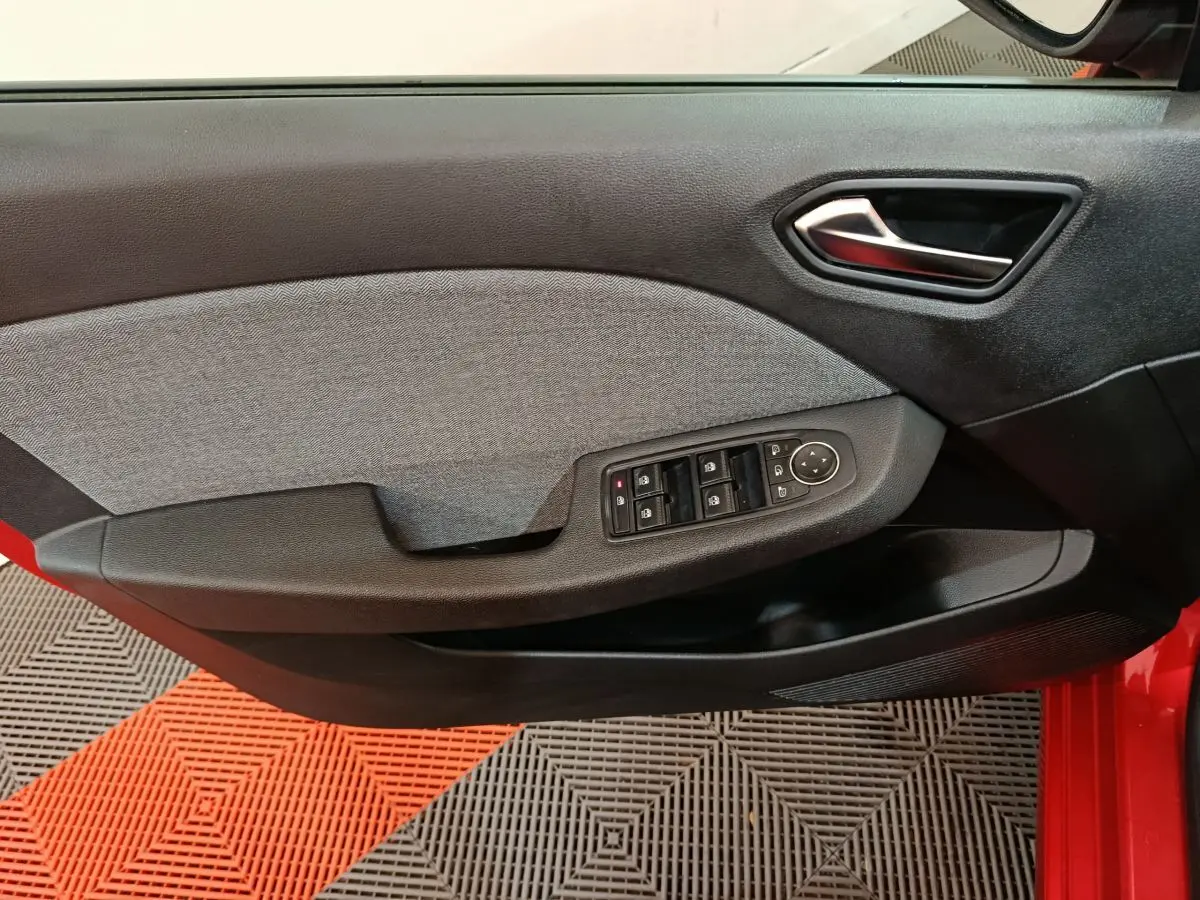 Vue rapprochée de la porte côté gauche rouge de la Renault Clio 2024 avec commandes électriques des vitres et poignée intérieure noire.