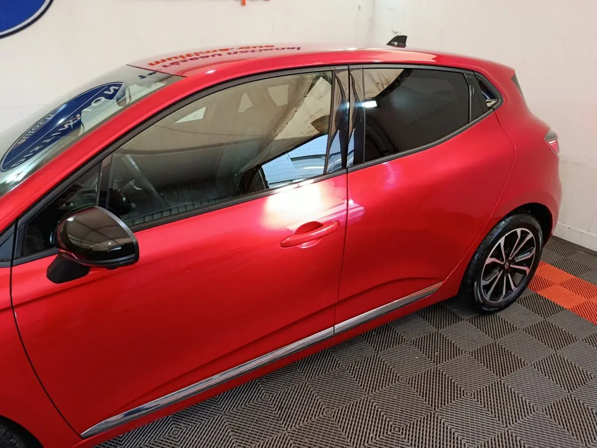 Profil côté gauche de la Renault Clio Techno TCe 90 rouge 2024 avec rétroviseur noir et jantes alliage visibles.