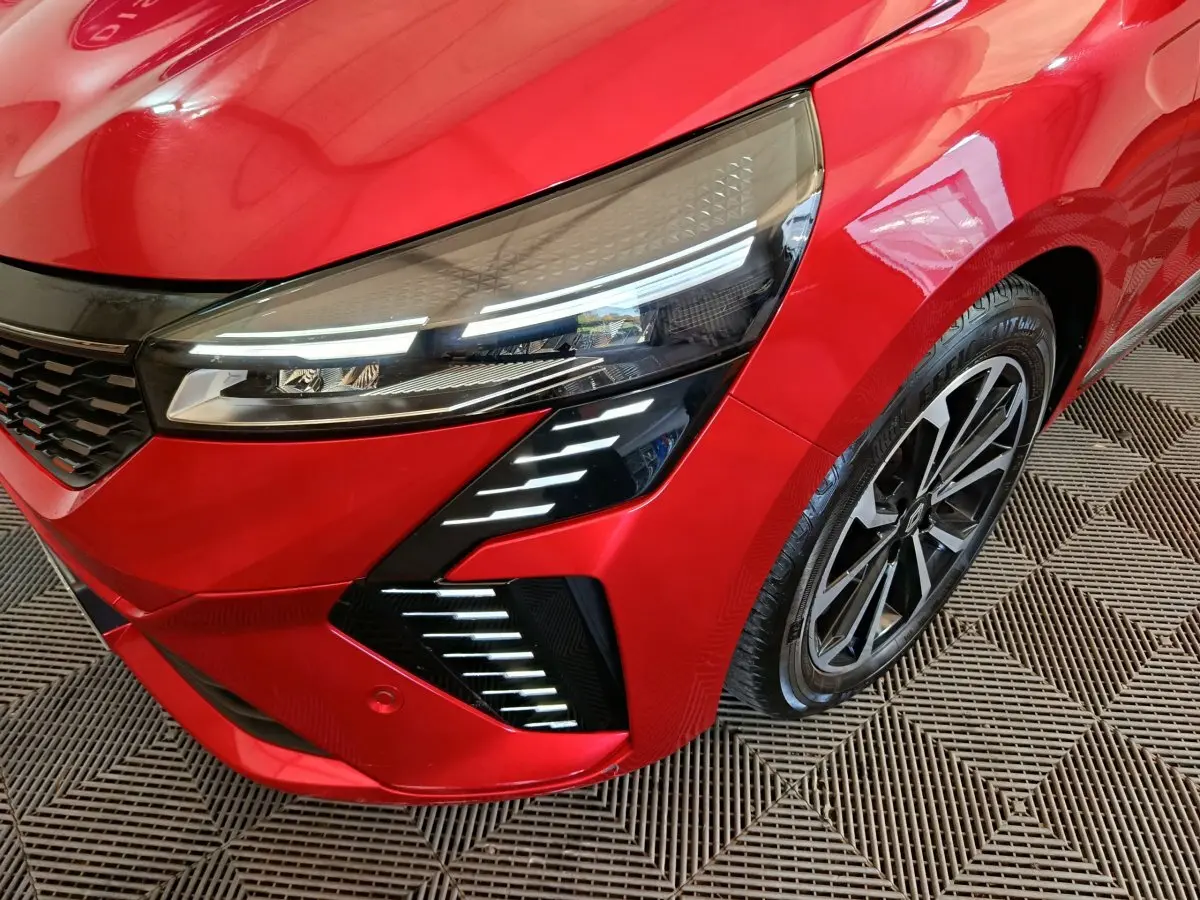 Gros plan sur l'avant droit rouge de la Renault Clio 2024 avec phares LED et jante alliage distinctive.