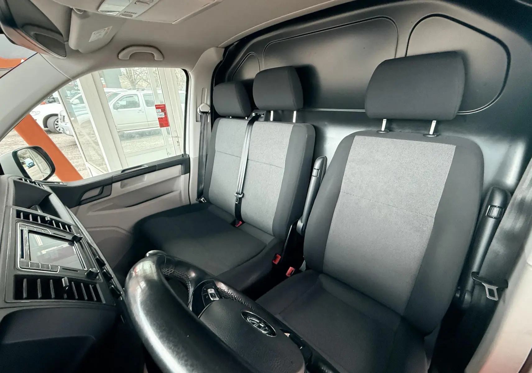 Vue intérieure côté conducteur du Volkswagen Transporter L1H1 2018, montrant les sièges avant gris et noirs et le tableau de bord.