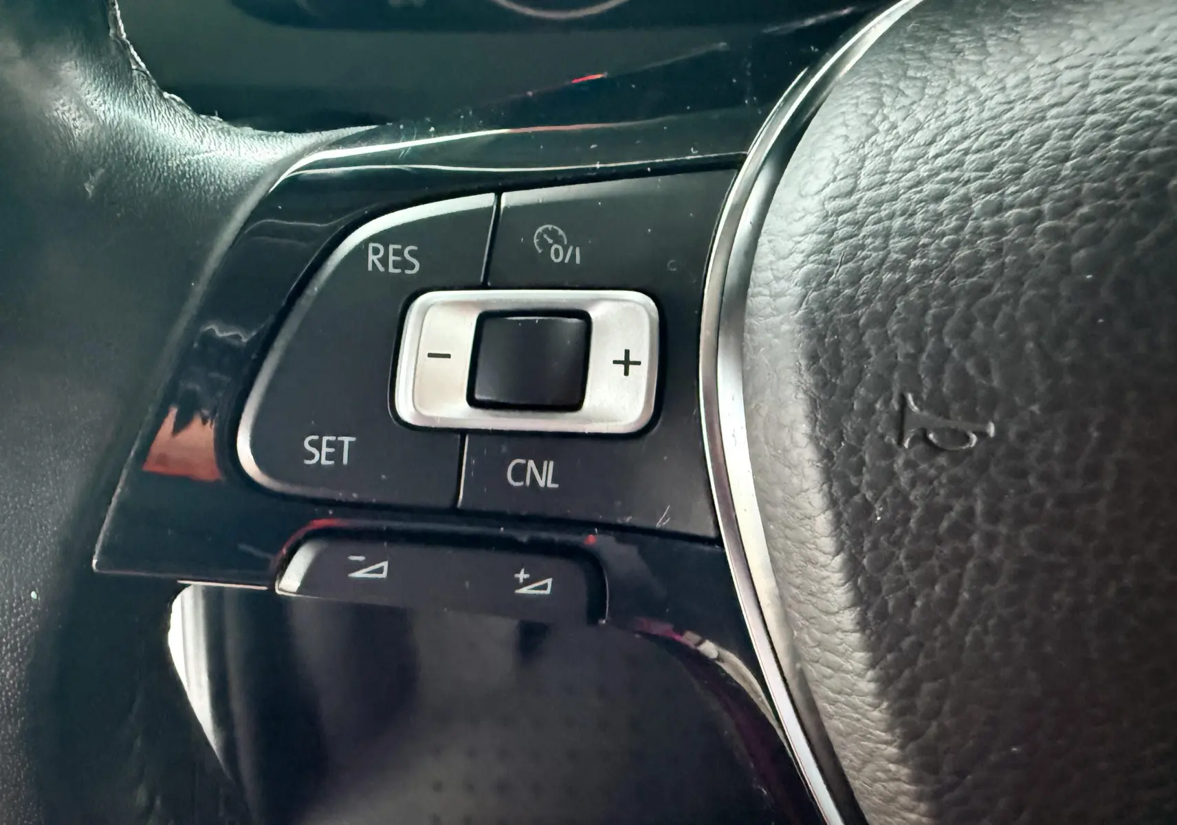 Gros plan sur les commandes de régulateur de vitesse à gauche du volant en cuir d’un Volkswagen Transporter blanc de 2018.