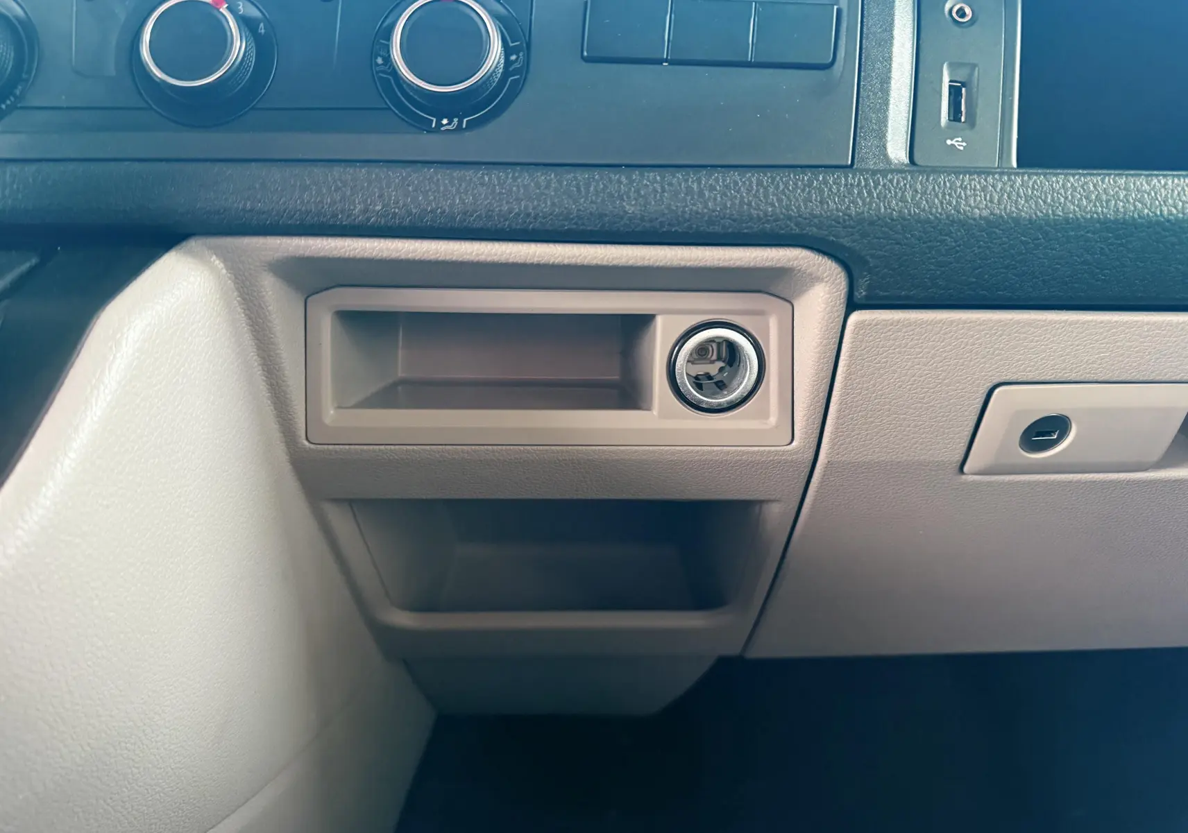 Détail de la console centrale beige du Volkswagen Transporter L1H1 2018, avec prise allume-cigare visible.